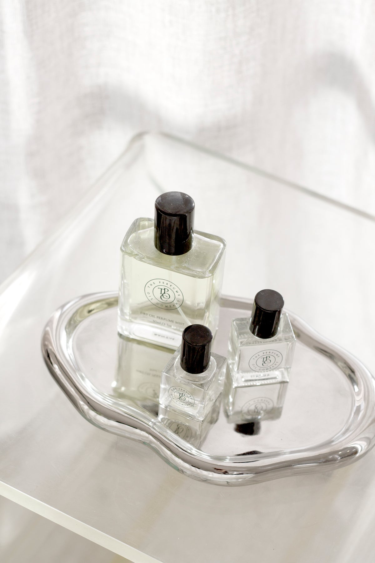Silver cloud tray holding three perfume bottles on a clear acrylic side table