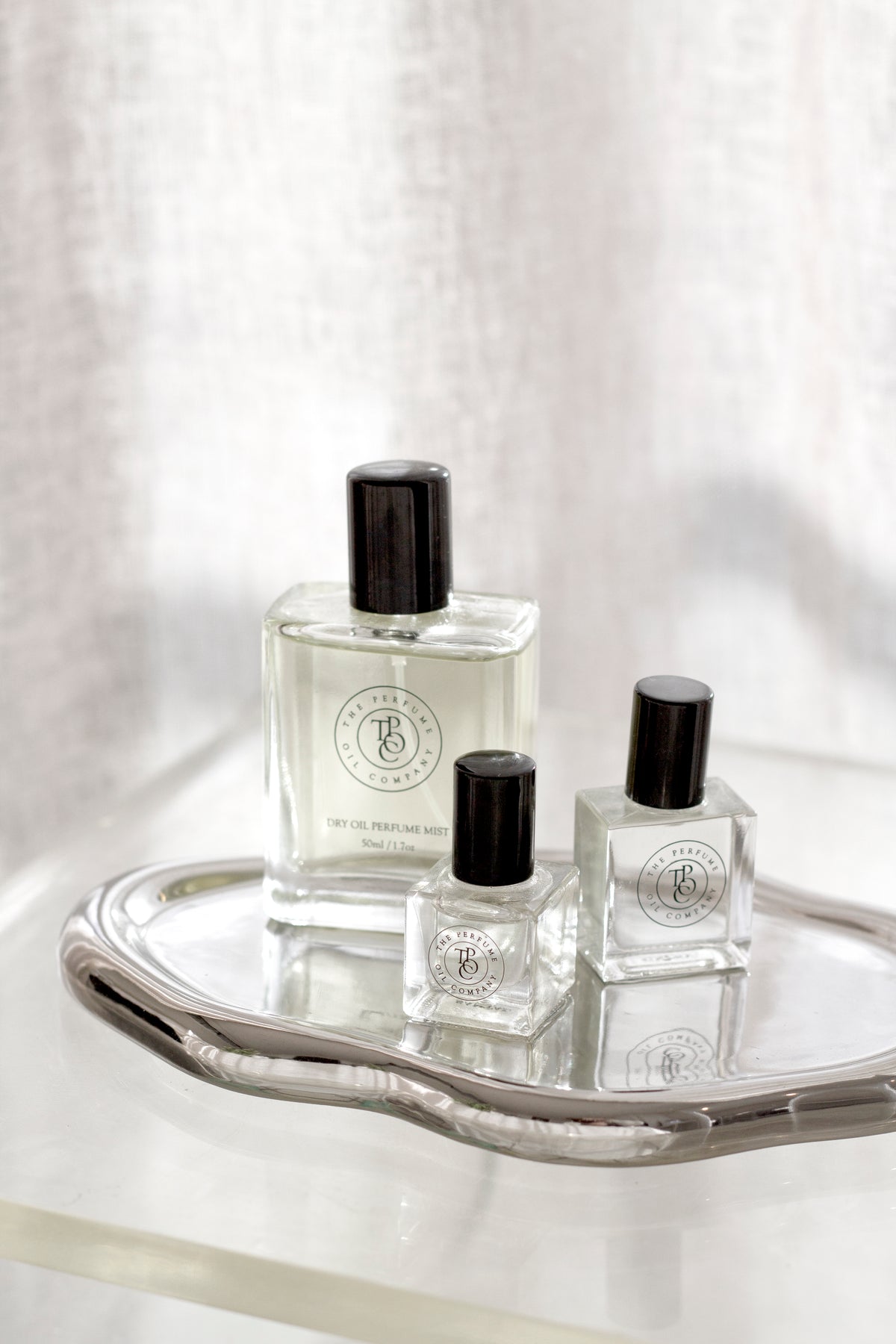 Silver cloud tray holding three perfume bottles of different sizes against a soft linen backdrop