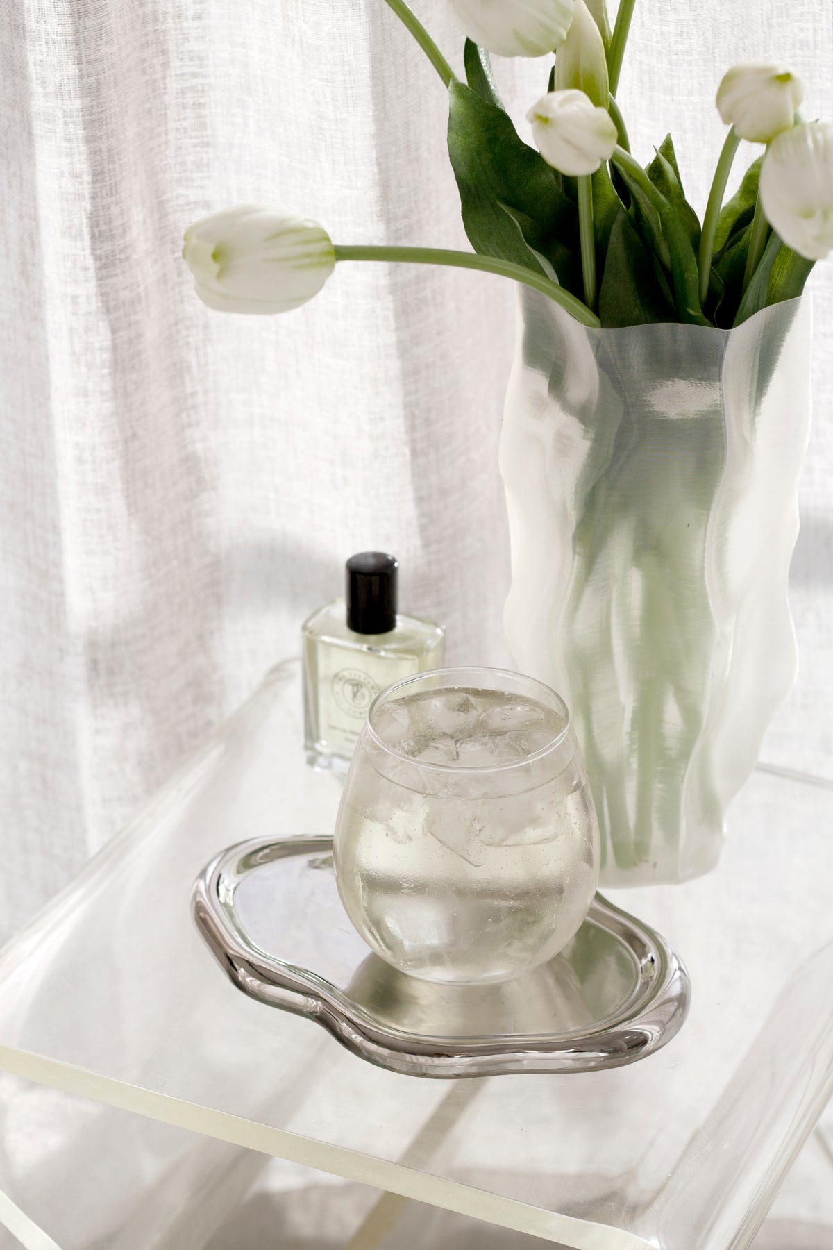 Silver cloud tray holding a glass carafe and perfume bottle beside white tulips in a frosted vase