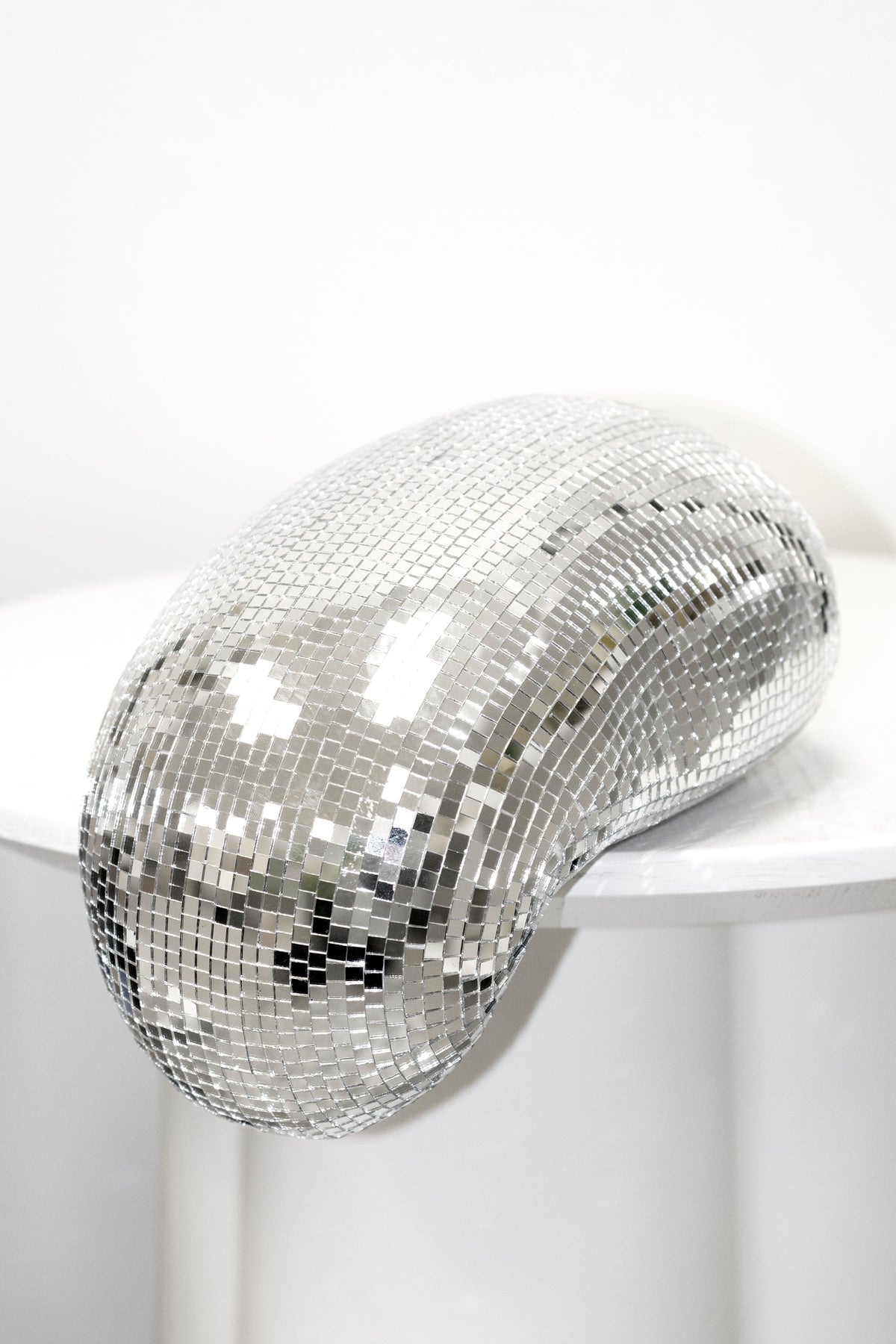 Melting disco ball on a white surface, catching light across the mirror tiles