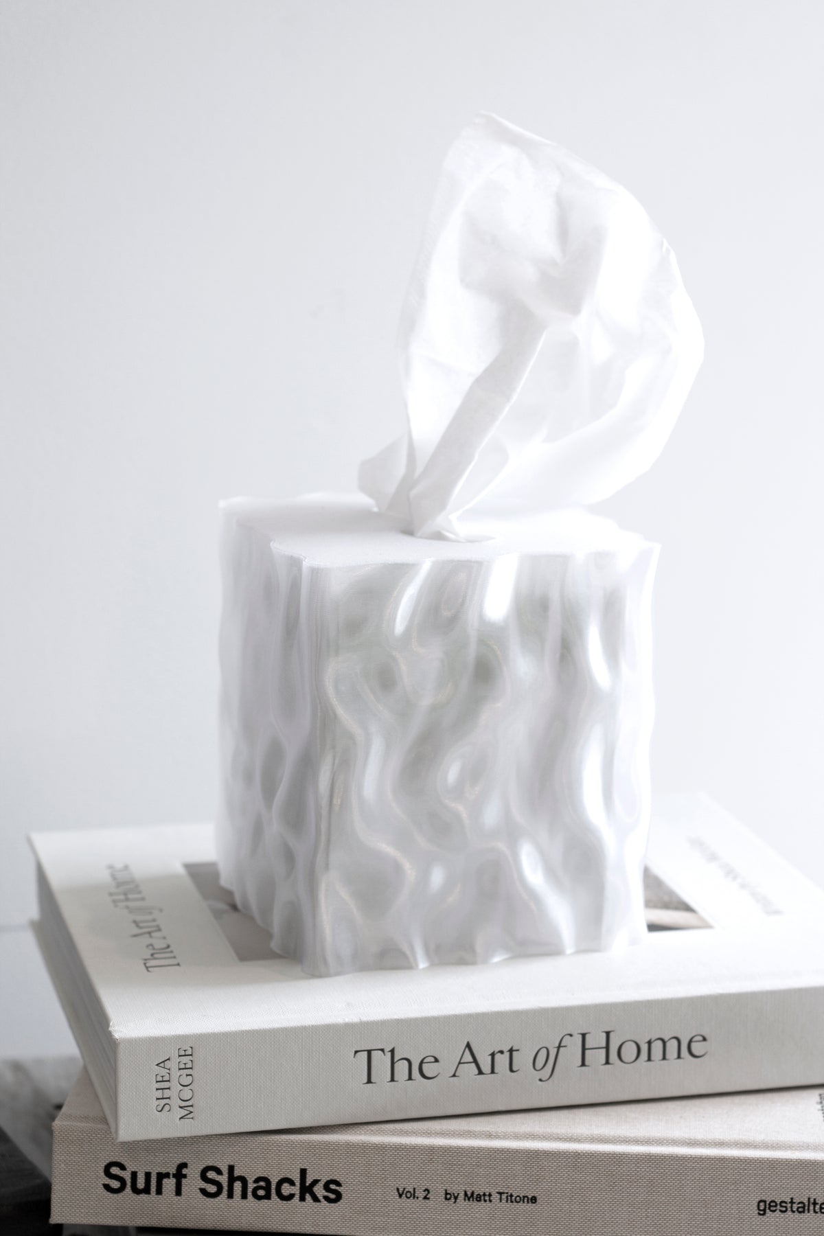 White Flow tissue box cover on a stack of books against a pale wall
