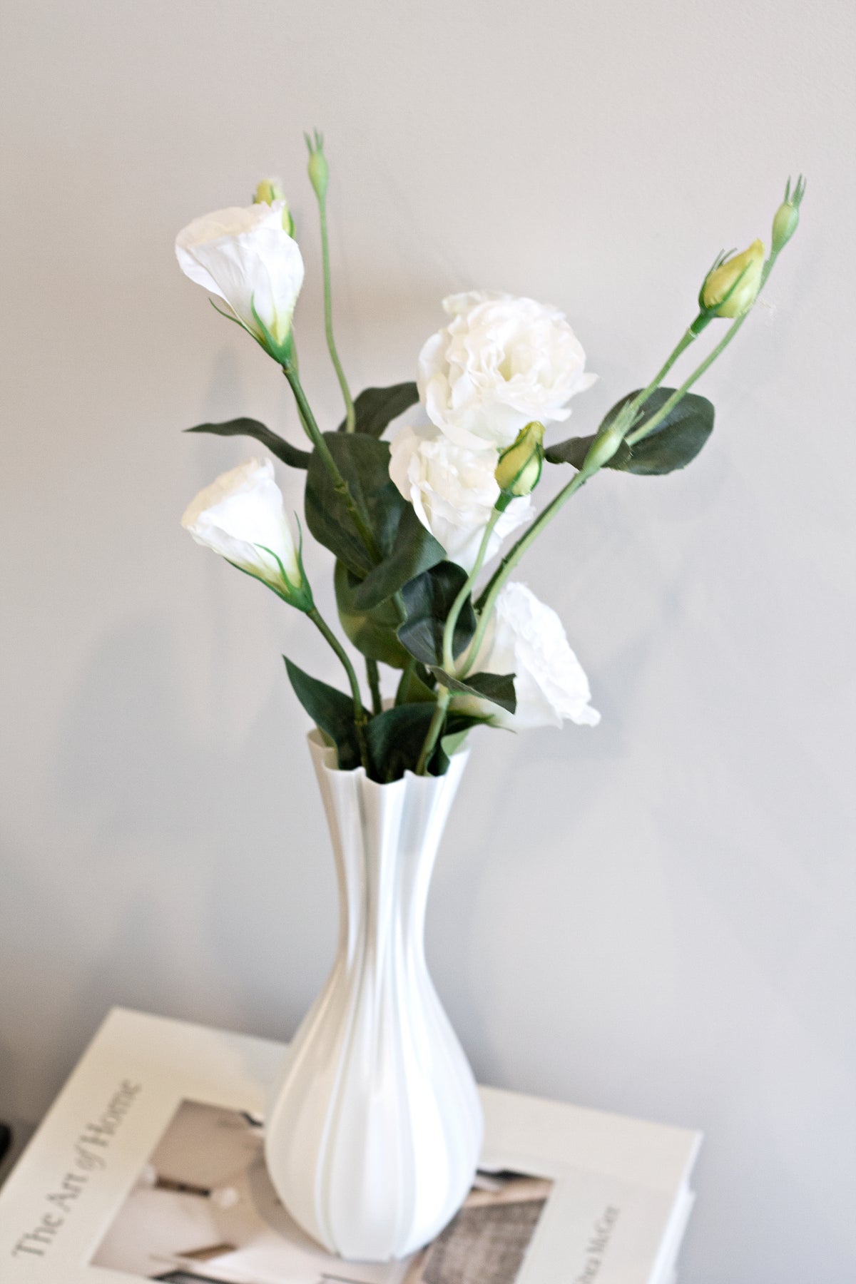Fluted white vase of white lisianthus resting on stacked books against a soft grey wall