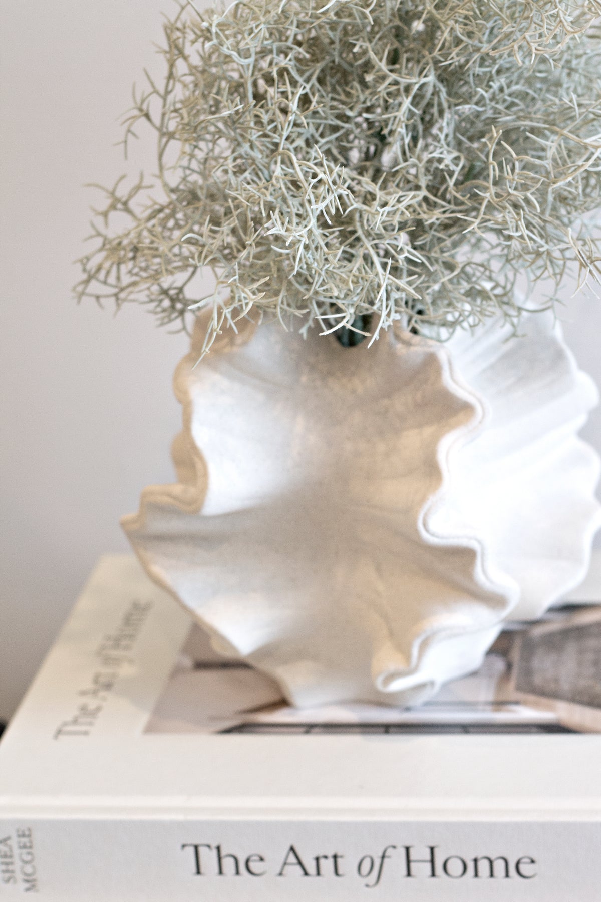Close on the coral vase's ruffled rim with grasses rising from the opening