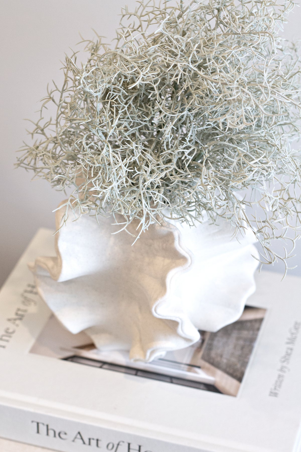 Coral vase of dried grasses angled on a book stack in soft daylight