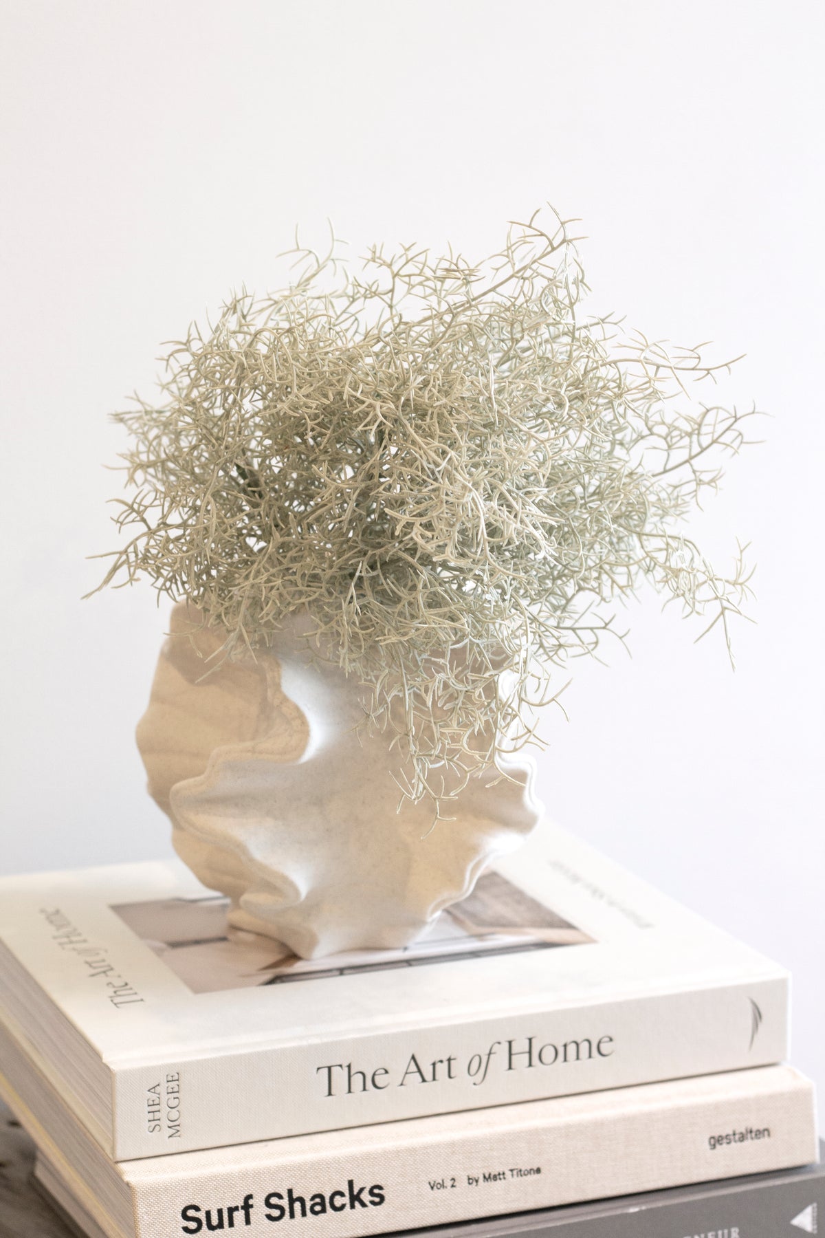 Pale dried grasses in the coral vase on a stack of design books