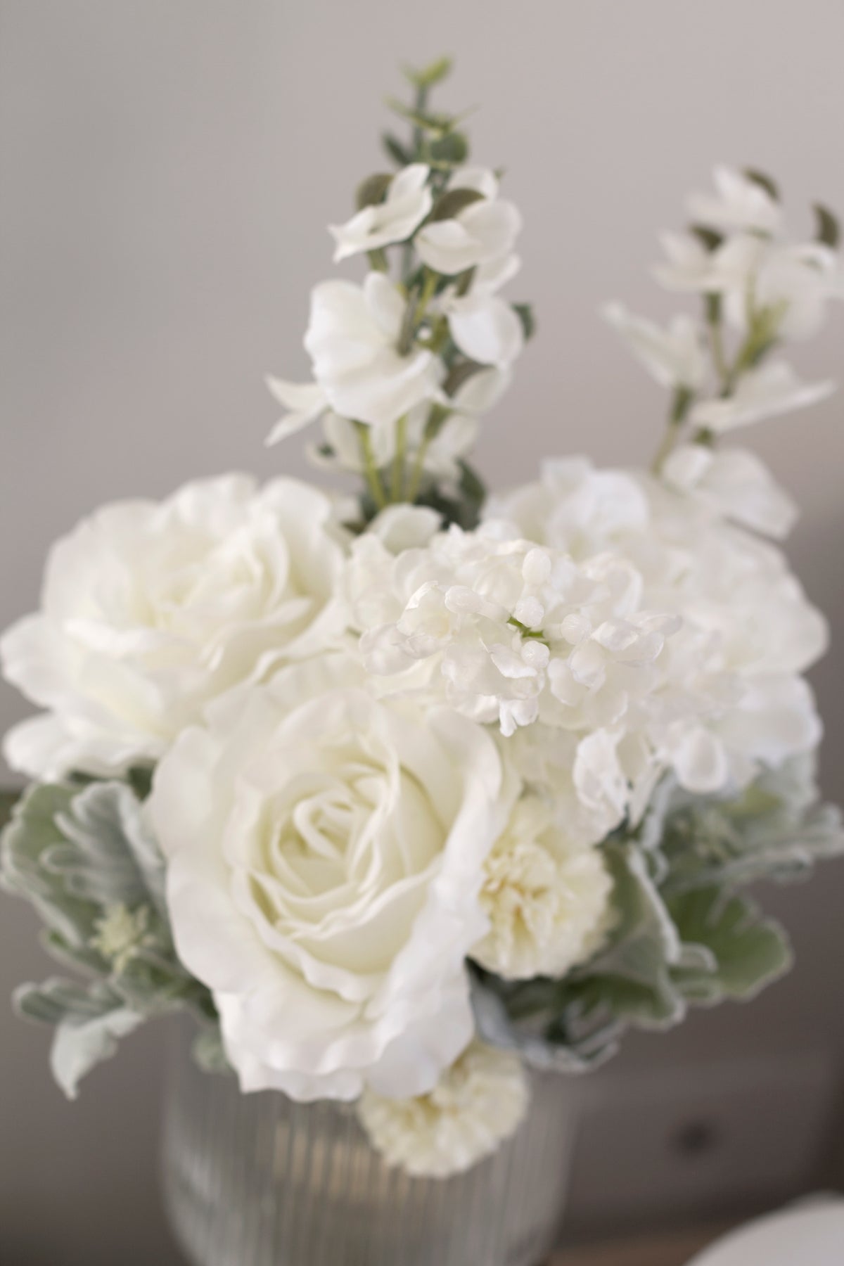 Close view of white faux roses and sweet peas in a textured vase