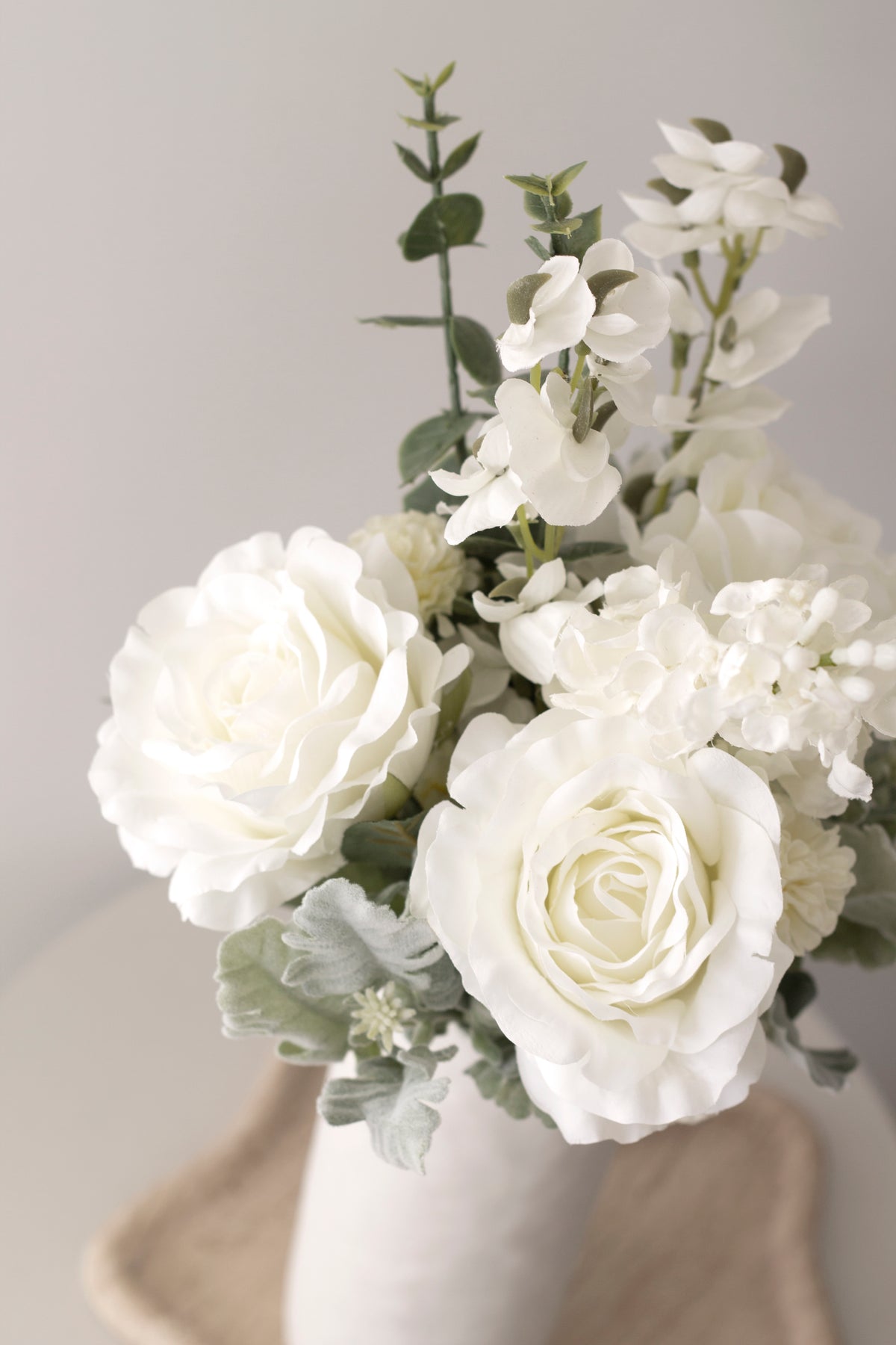 Close-up of white faux roses in a textured white vase