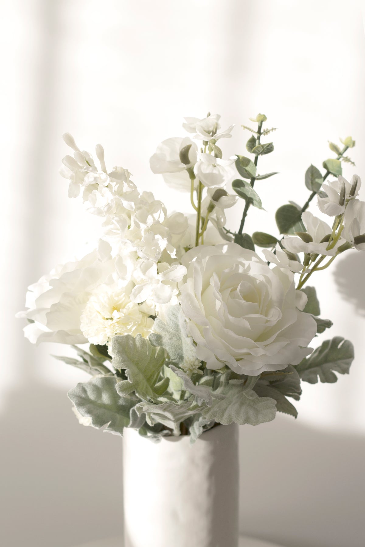 White faux roses and foliage in a small white vase