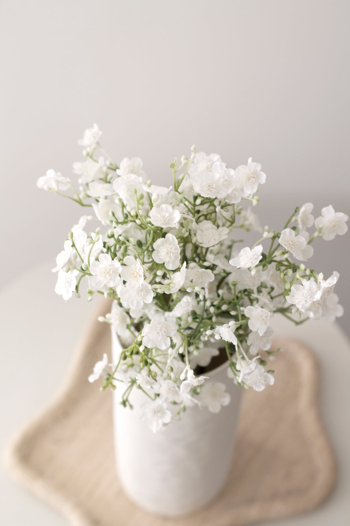 Faux gypsophila in a sculpted cream vase on a table