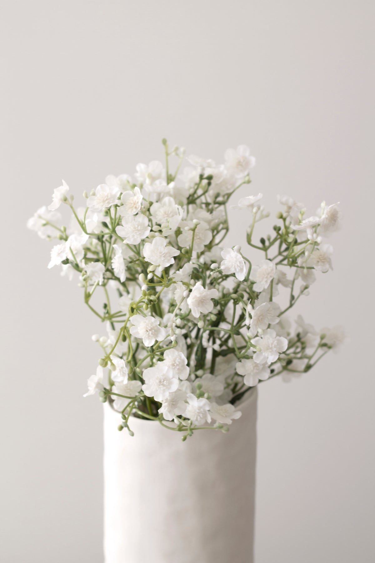 Faux gypsophila in a textured white vase in a bright room