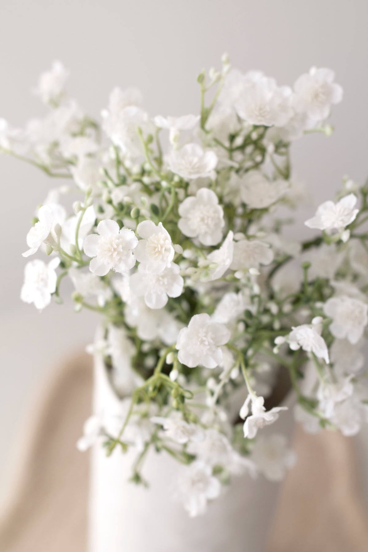 Faux gypsophila filling a white vase beside a chair