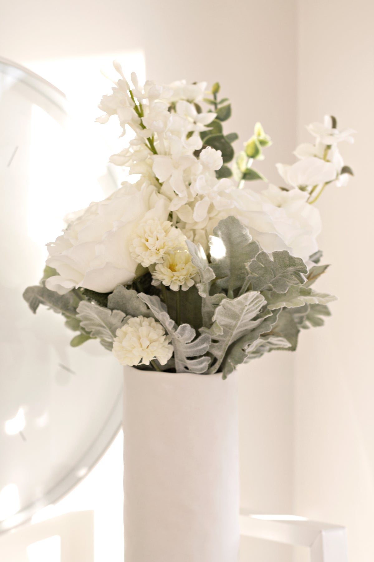 White faux bouquet in a tall white vase on a pale shelf