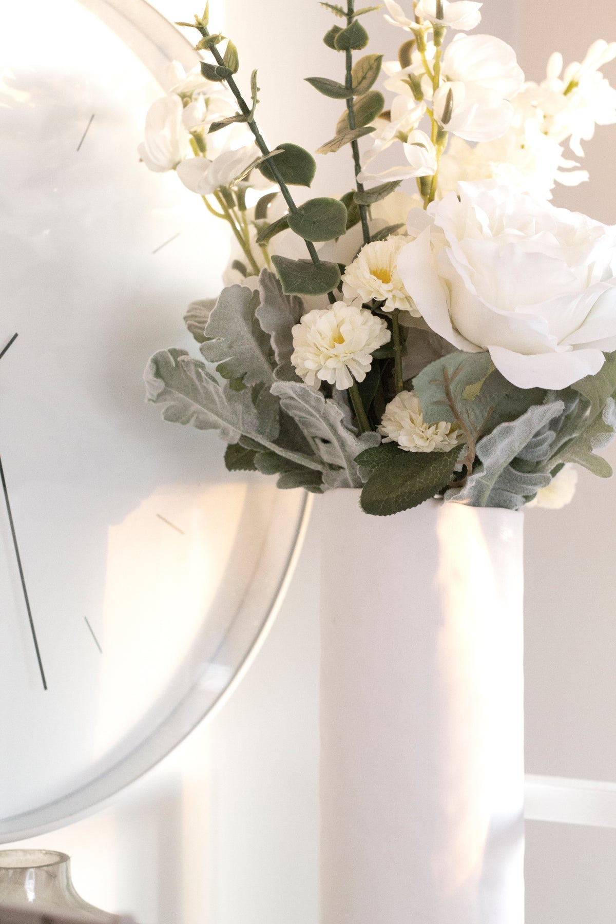 White faux bouquet with eucalyptus beside a round mirror