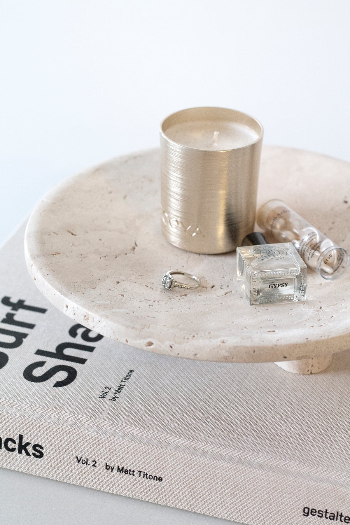 Side view of a Nome stand with a gold candle, perfume and rings on a coffee table book
