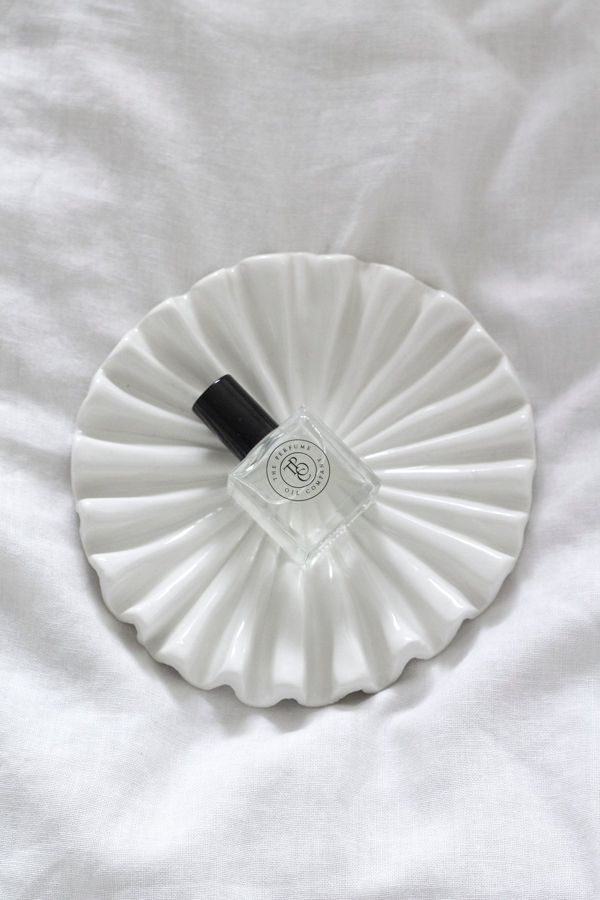 Top-down view of a perfume bottle on the fluted tray on white linen