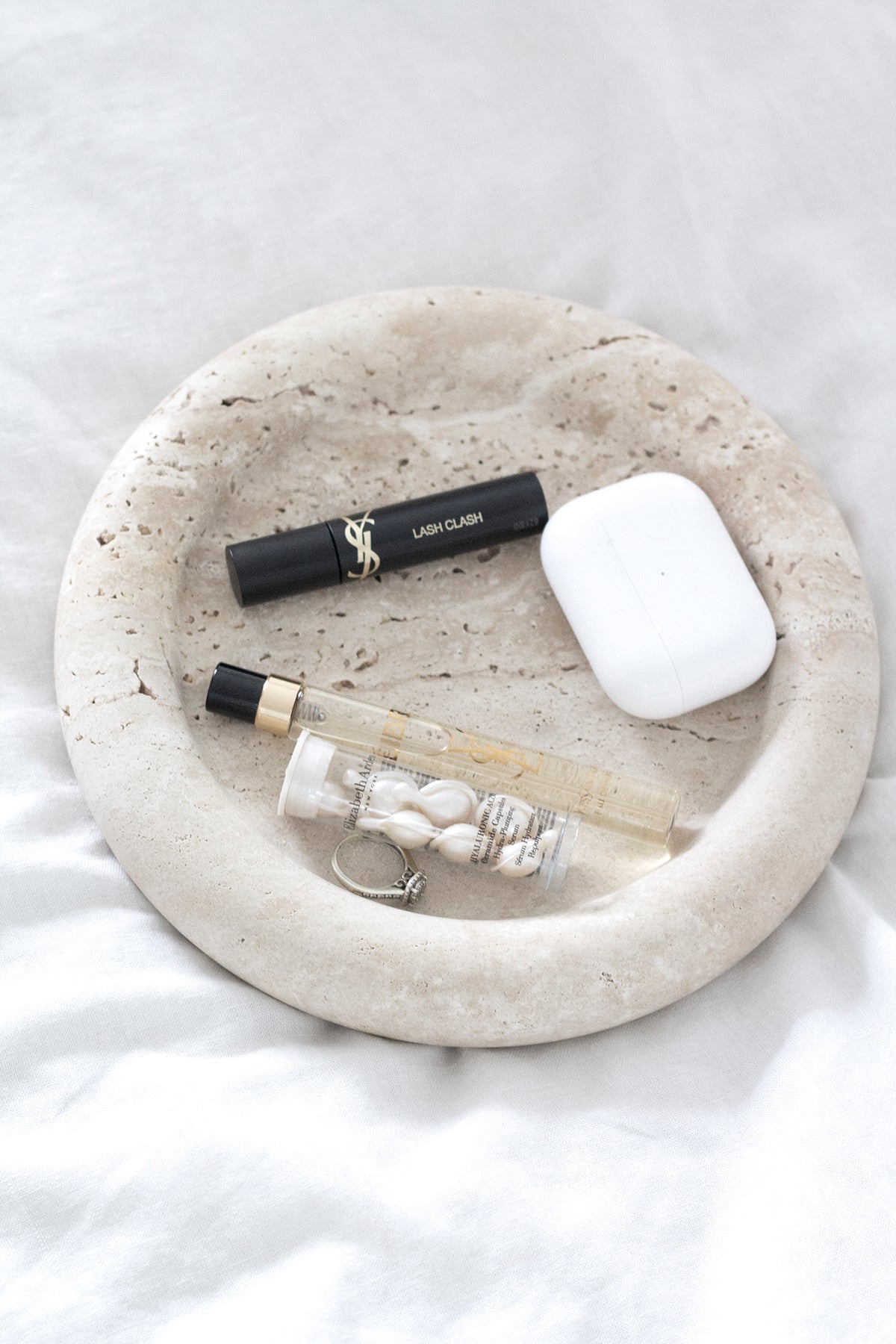 Bay Round Tray holding mascara, an earbuds case and a perfume oil on white bedding