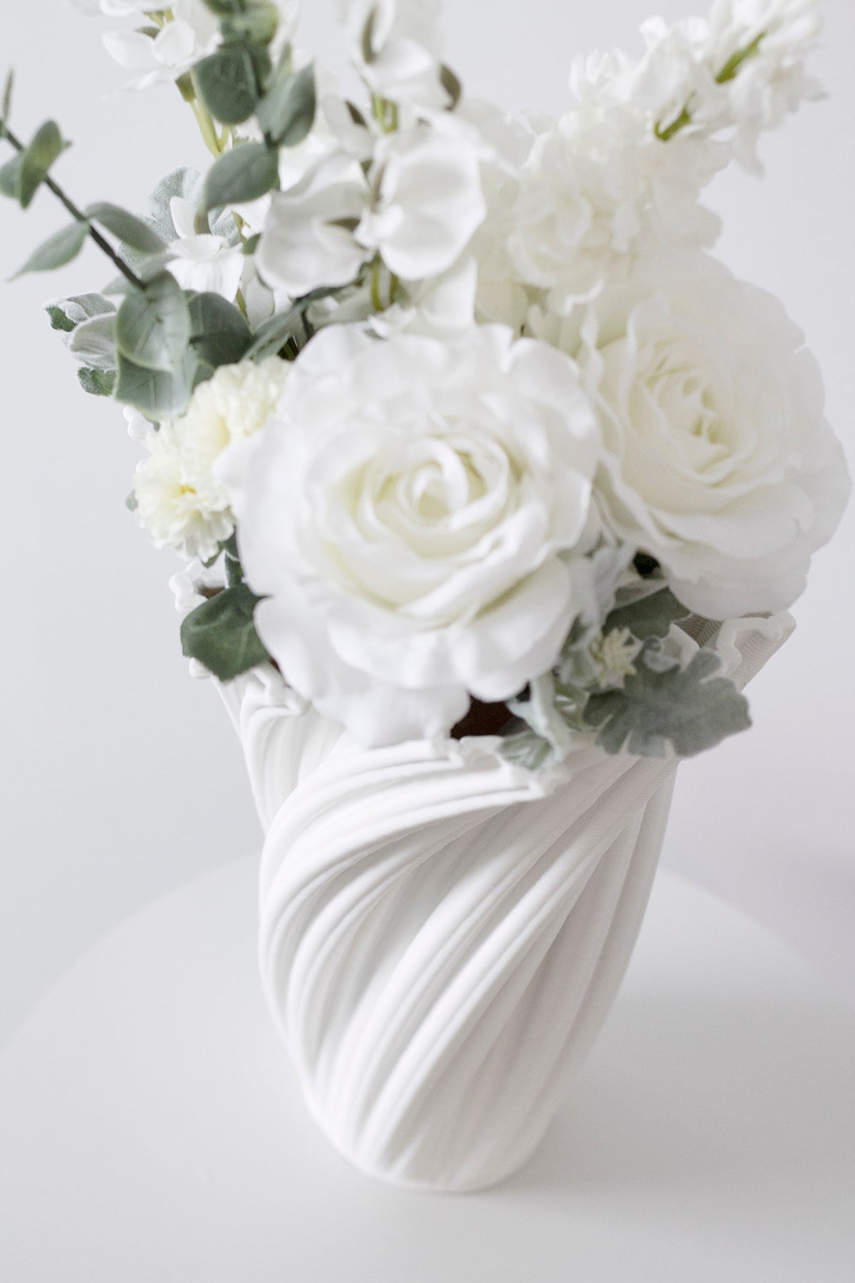 White faux bouquet in a white swirl vase in soft light