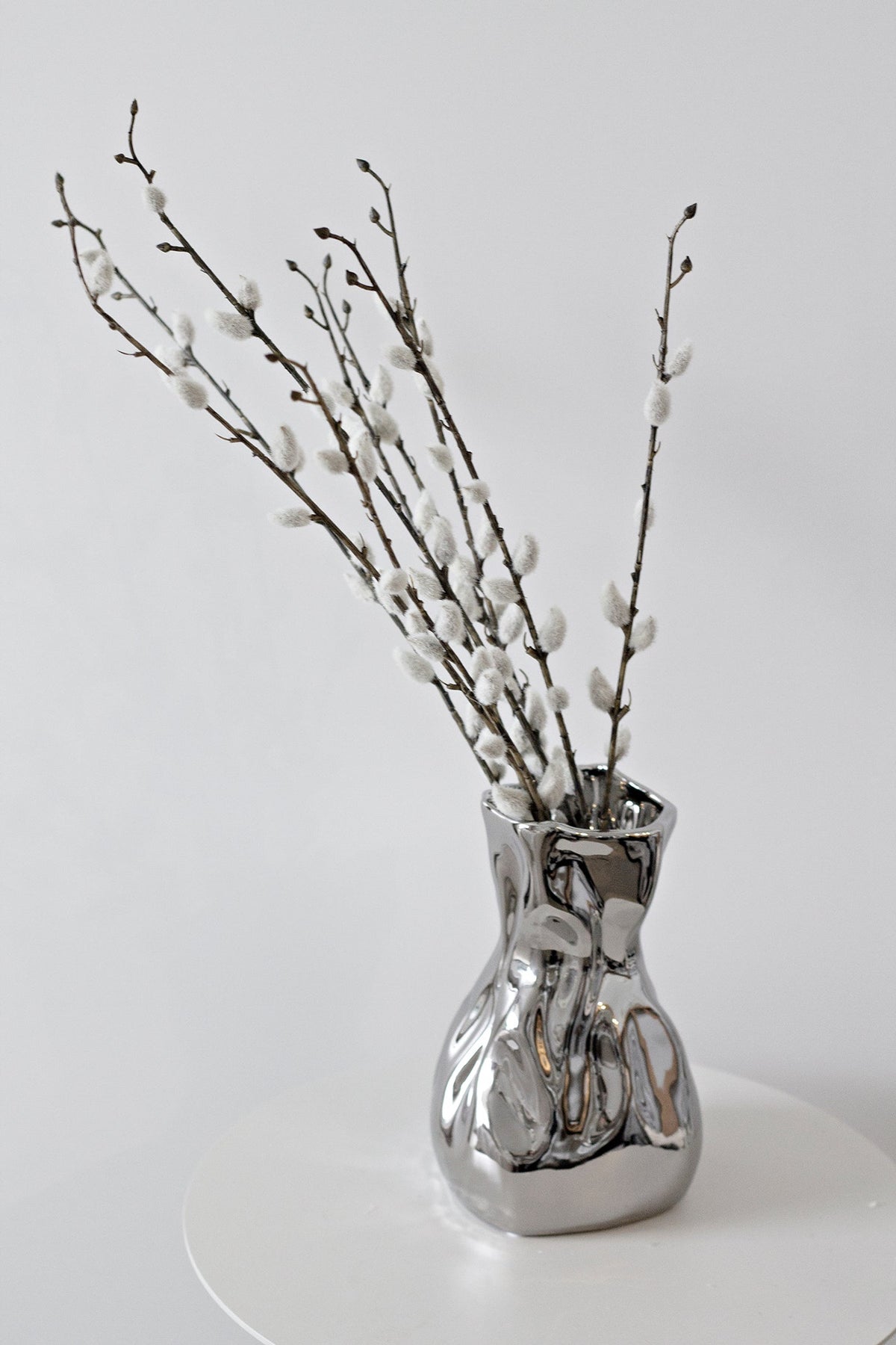 Faux pussy willow stems in a crumpled silver vase
