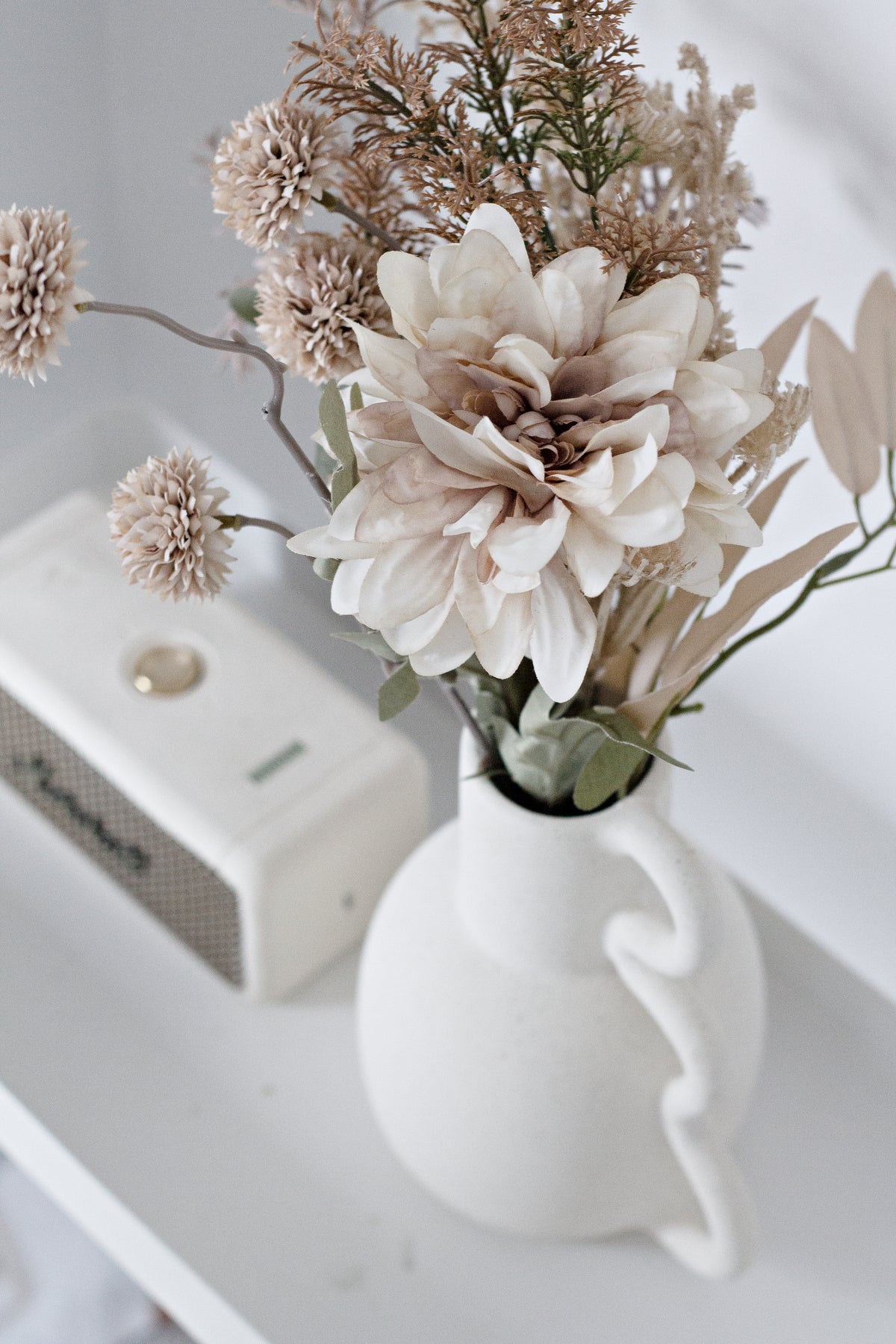 Chloe vase of blush dried florals beside a small speaker on a white shelf