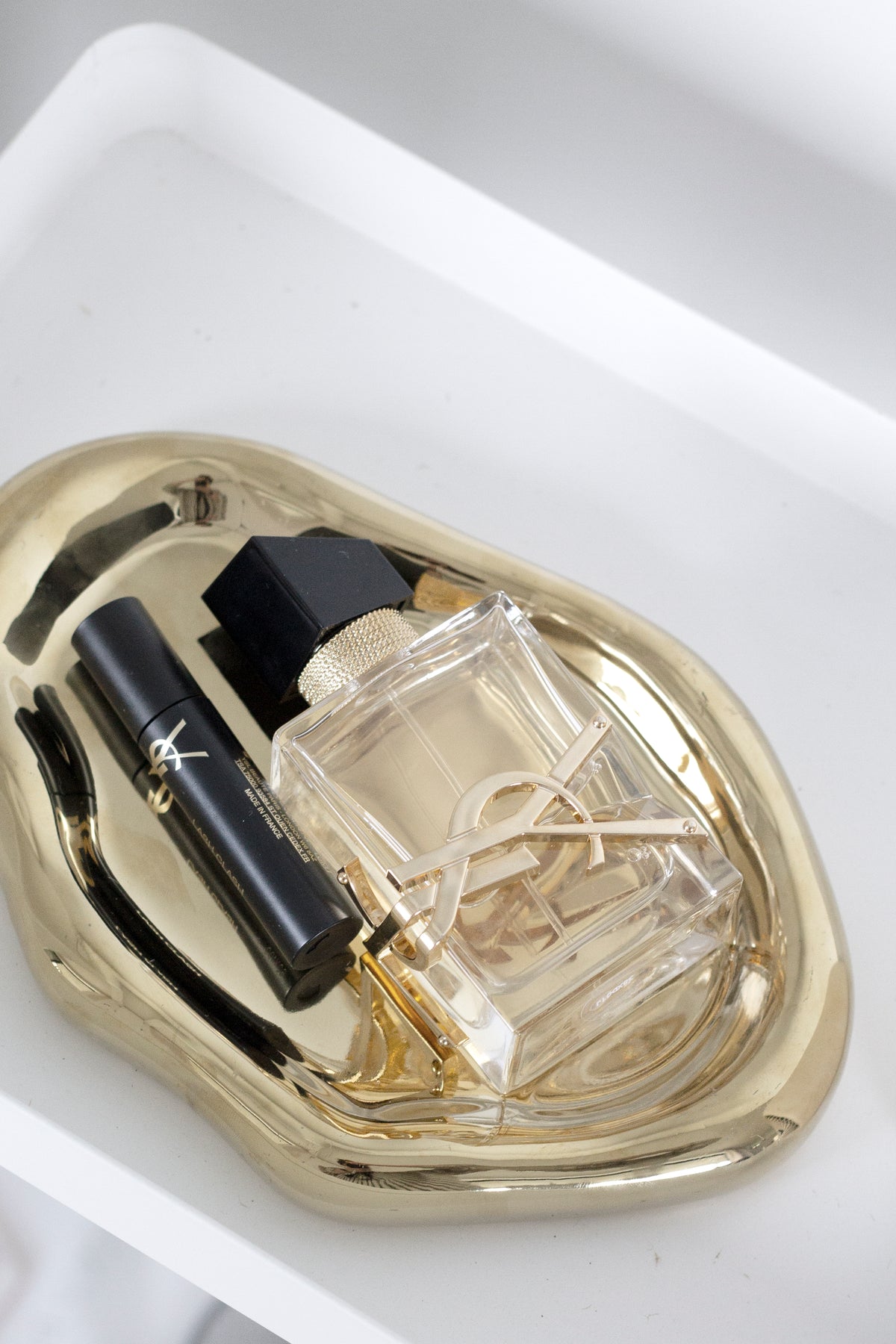 Overhead of the gold tray in a white niche, holding a glass perfume bottle and a slim black lipstick