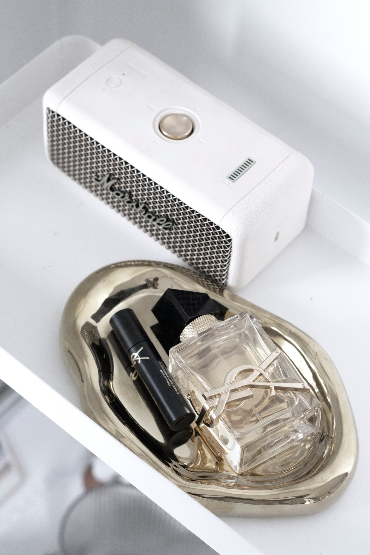 Gold cloud tray on a white shelf holding a square glass perfume bottle and a black lipstick tube