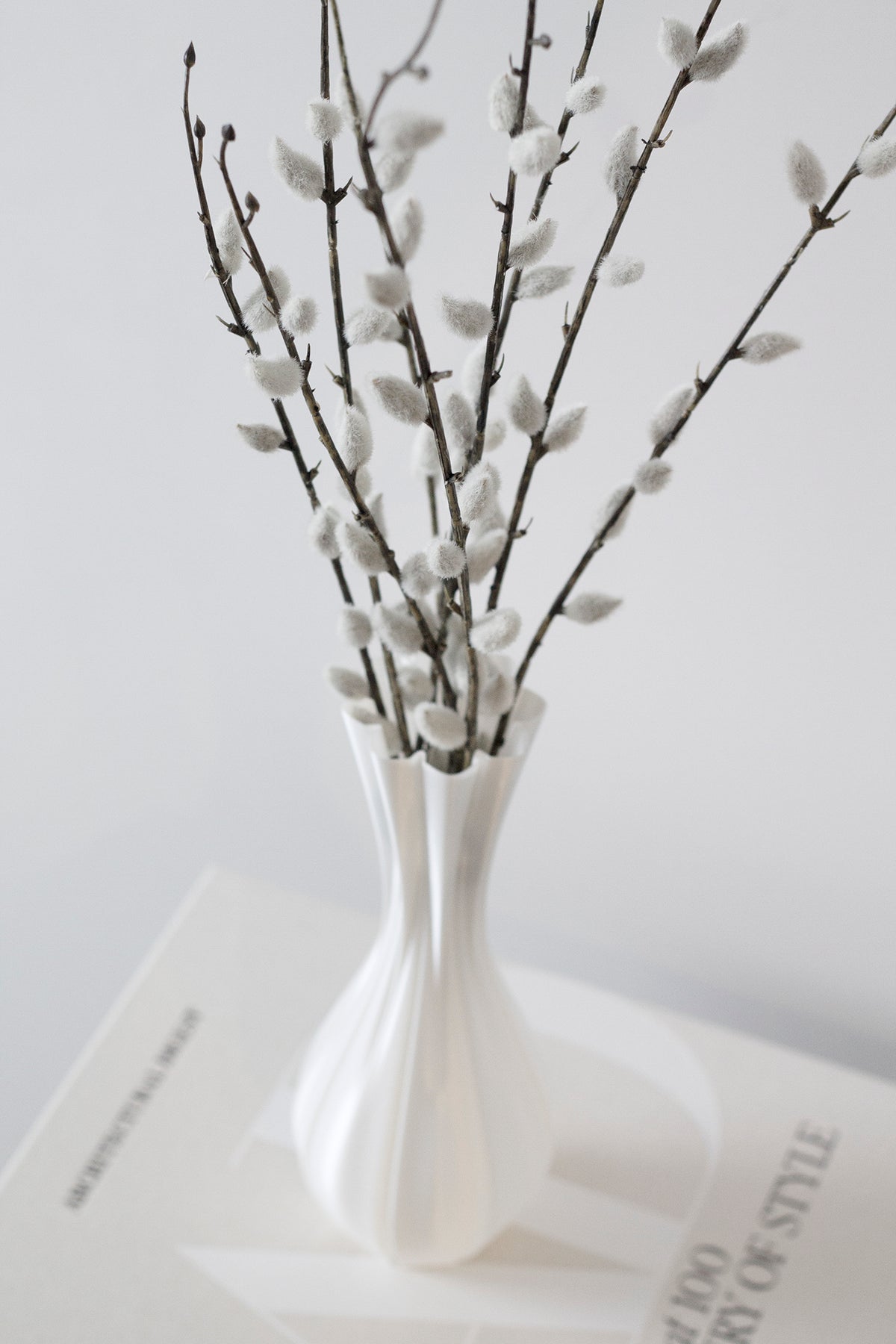 Faux pussy willow in a white ribbed sculptural vase on a coffee table book