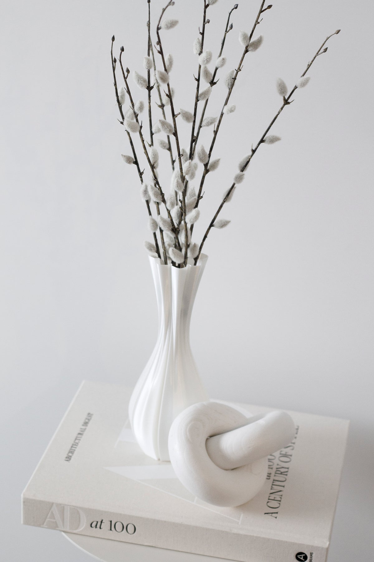 Natural wood knot sculpture beside a white ribbed vase of pussy willow on a book