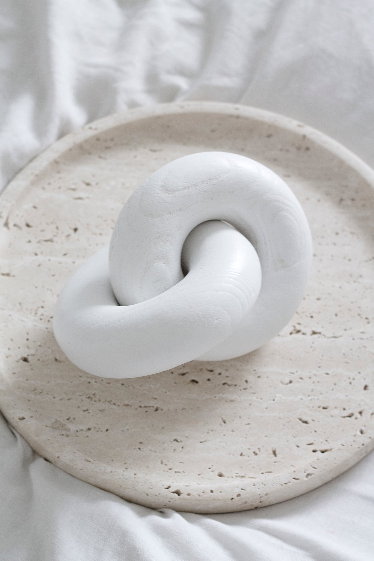 White wooden knot sculpture on a speckled travertine plate on white linen