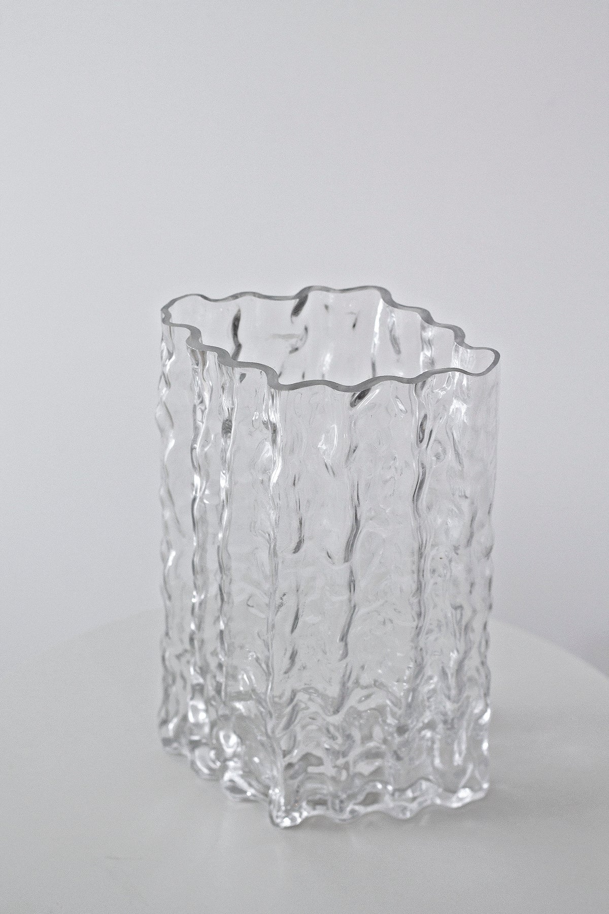 Clear Glacier vase shown empty on a pale surface, seen at three quarters