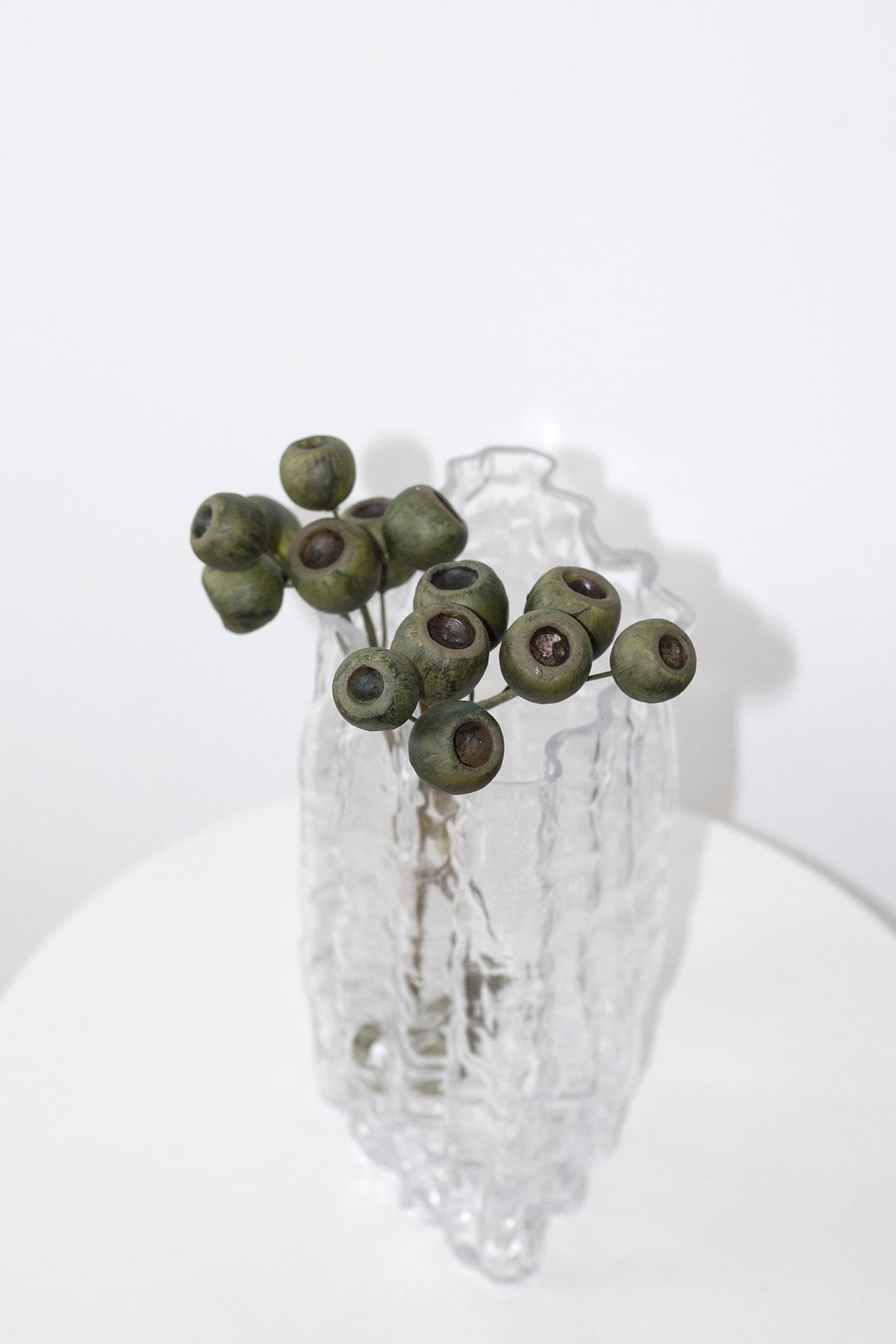 Clear Glacier vase holding eucalyptus gum nuts on a round white pedestal