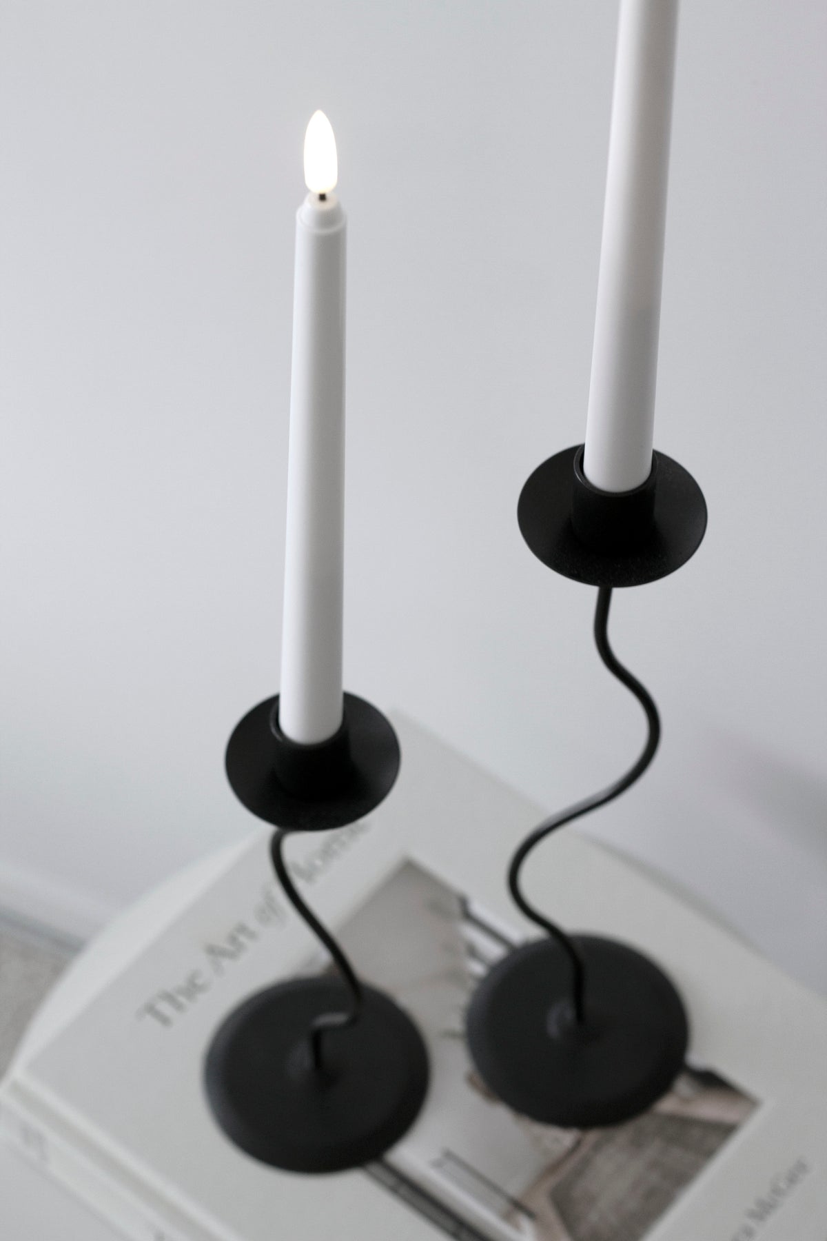 Close up of the black Hera pair with white tapers, one lit, on a stack of books
