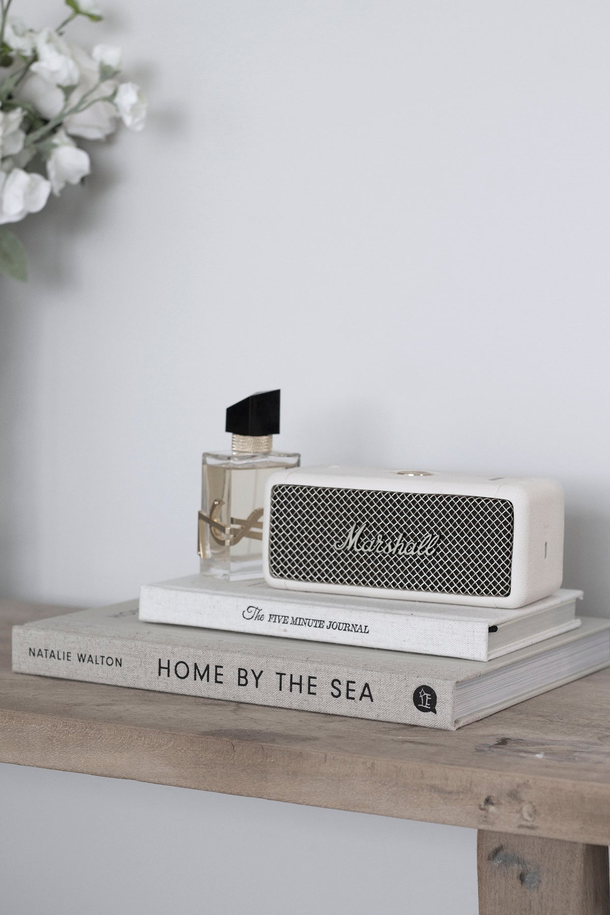 Alarm clock and stacked books beside white blossom on a pale ledge