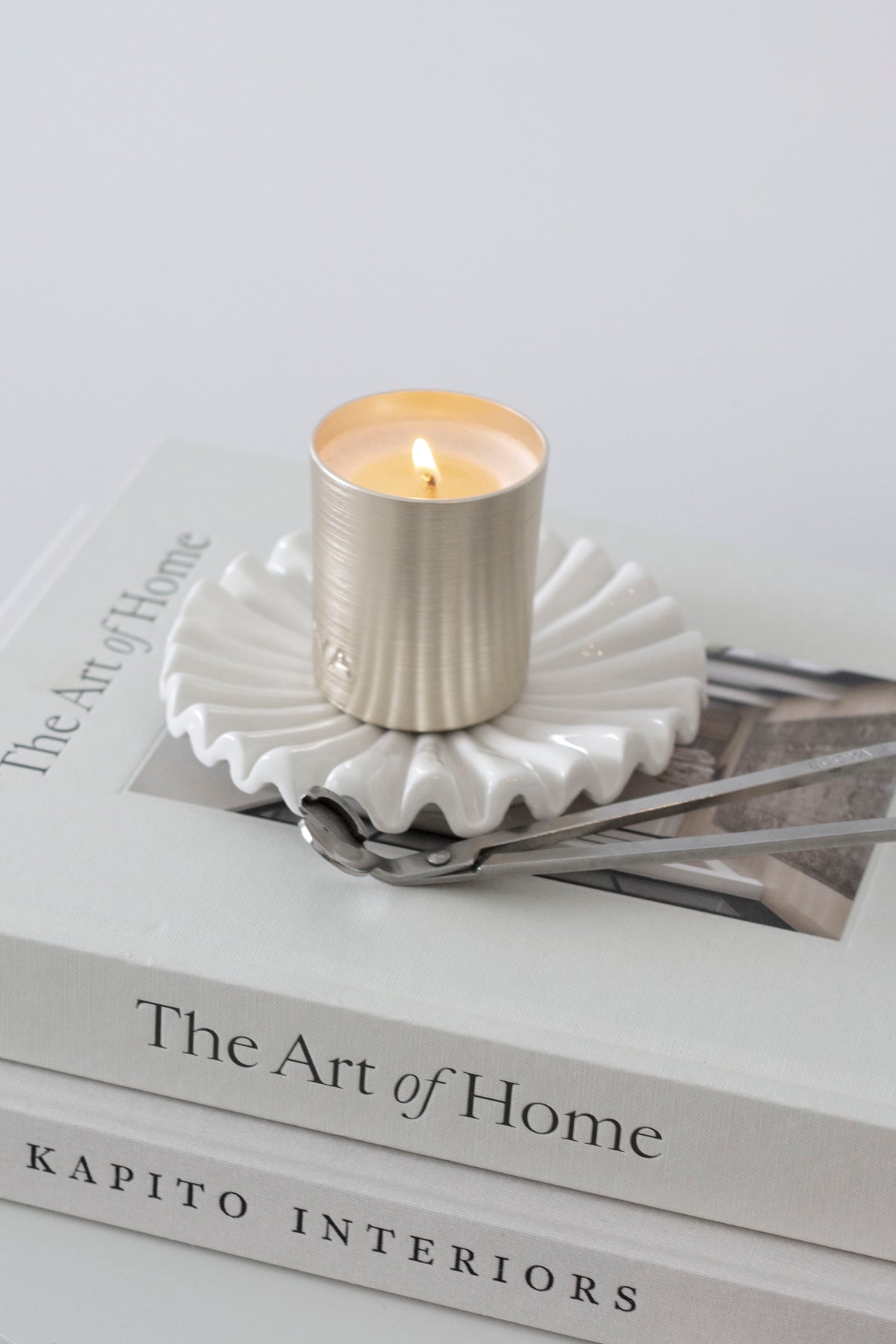The Art of Home in a book stack with a gold candle on a fluted white dish and a wick trimmer