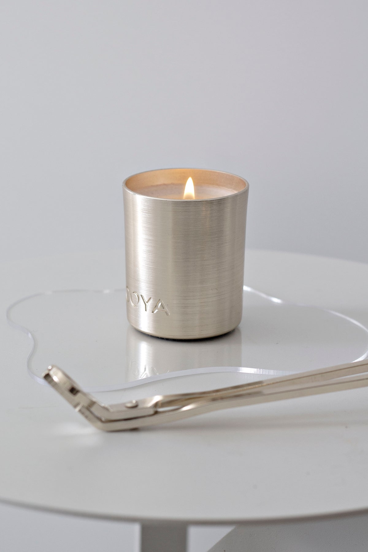 Silver wick trimmer trailing across a round white table beside a lit metallic candle