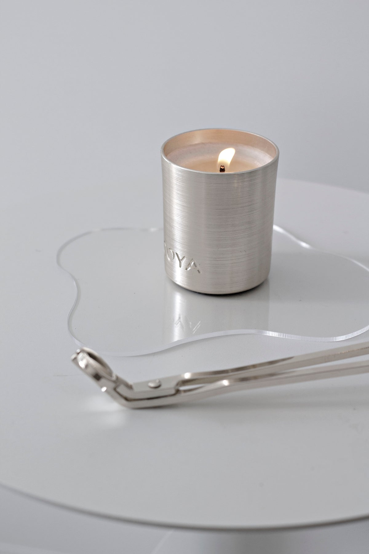 Silver wick trimmer beside a lit metallic candle on a round white side table
