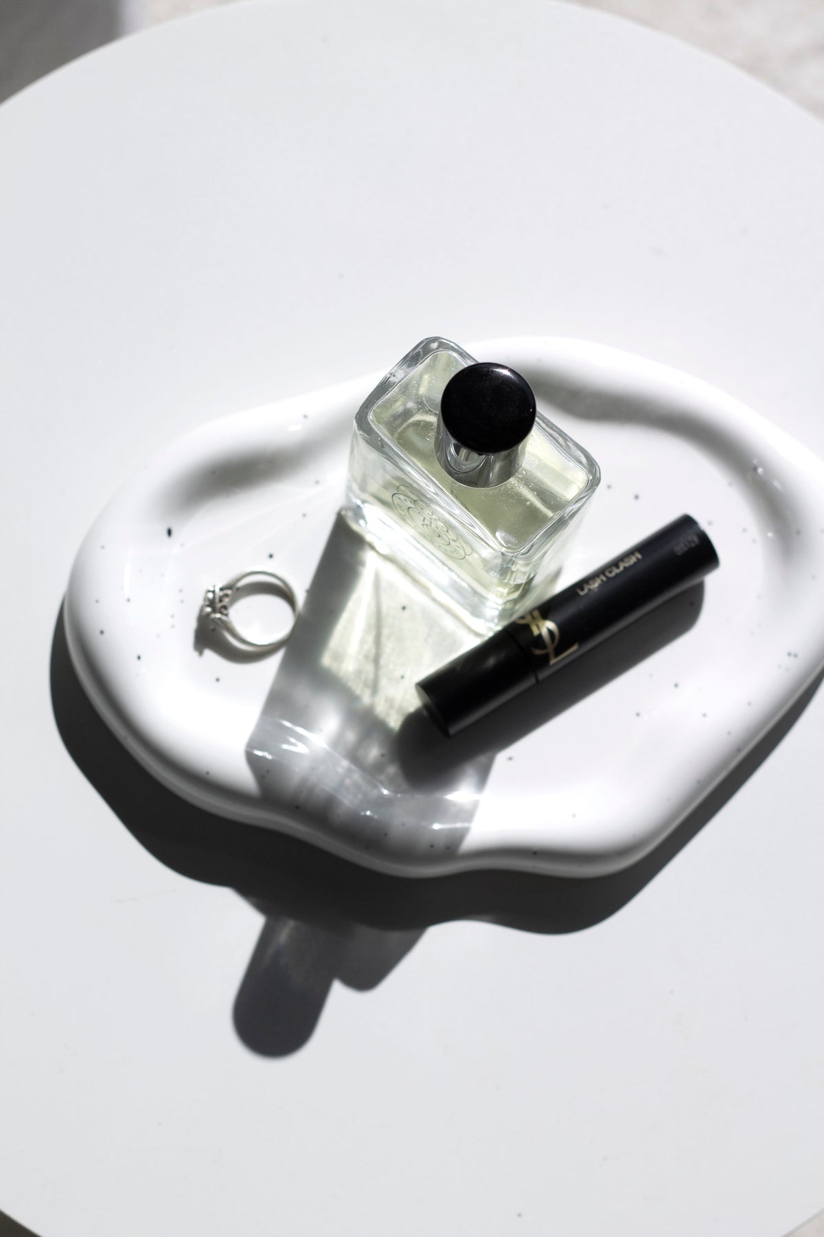 Speckled white cloud ceramic tray from above holding a perfume bottle, mascara and a ring
