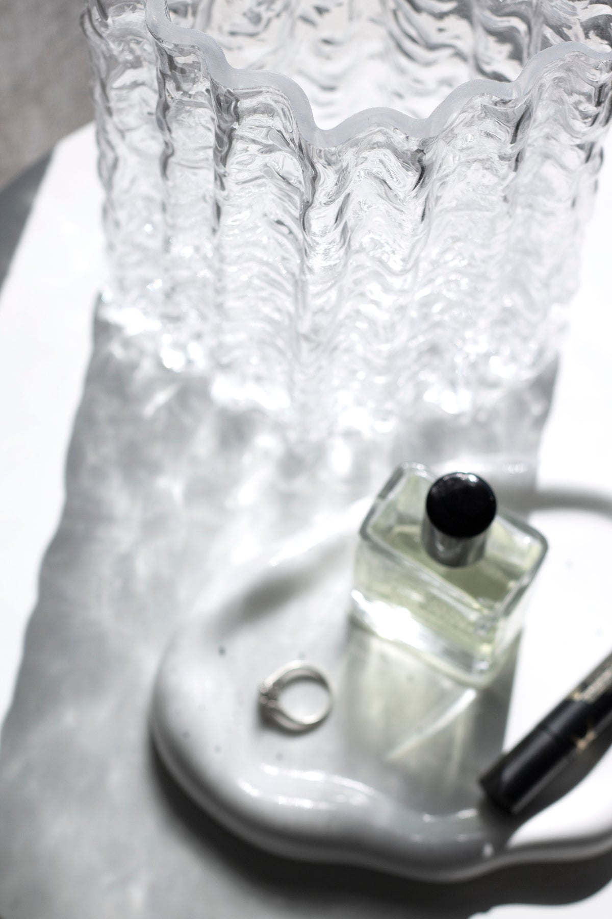 Close up of the clear Glacier vase base on a wavy dish beside a fragrance bottle and a ring