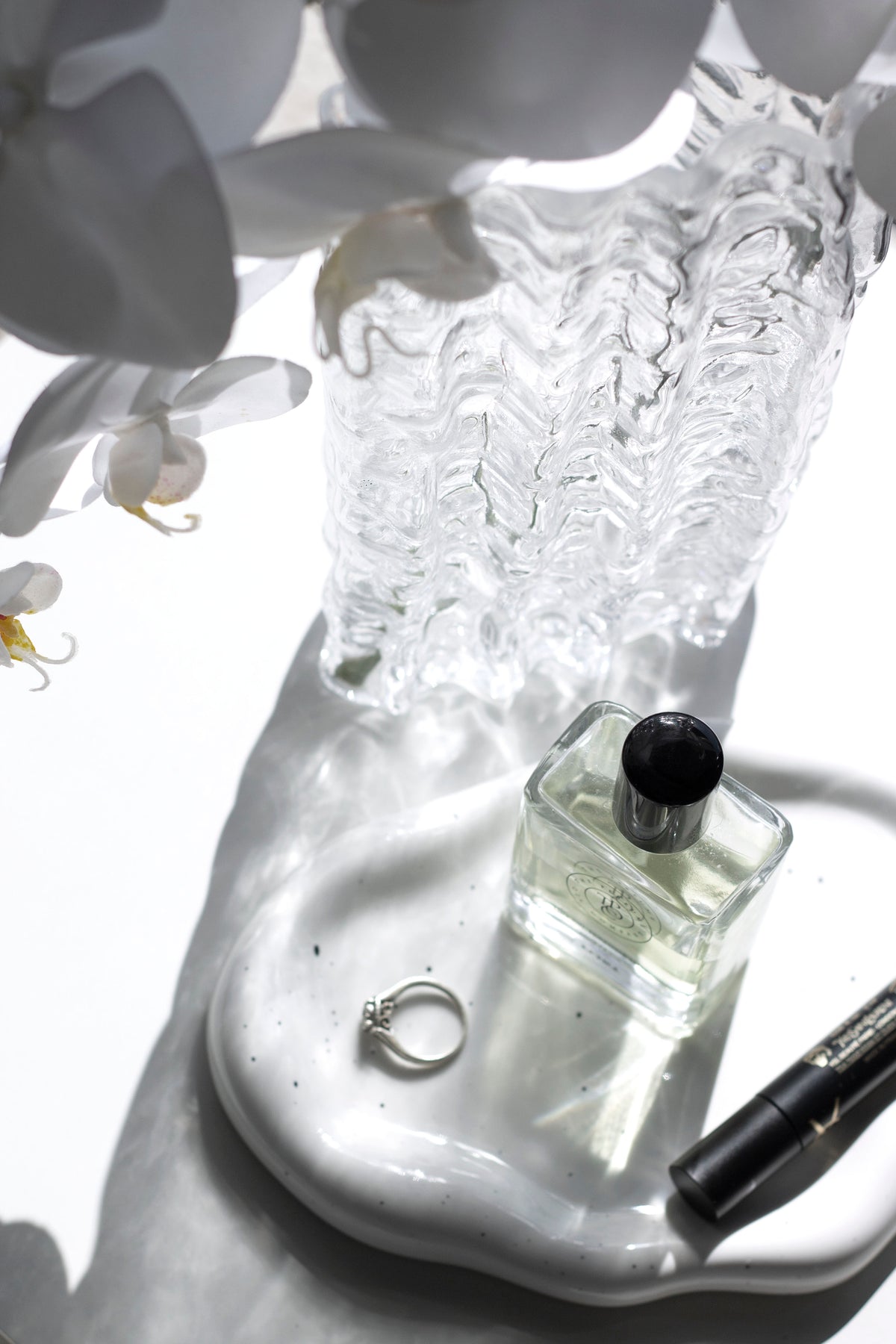 Speckled white cloud ceramic tray with a perfume bottle, ring and mascara beside a glass vase