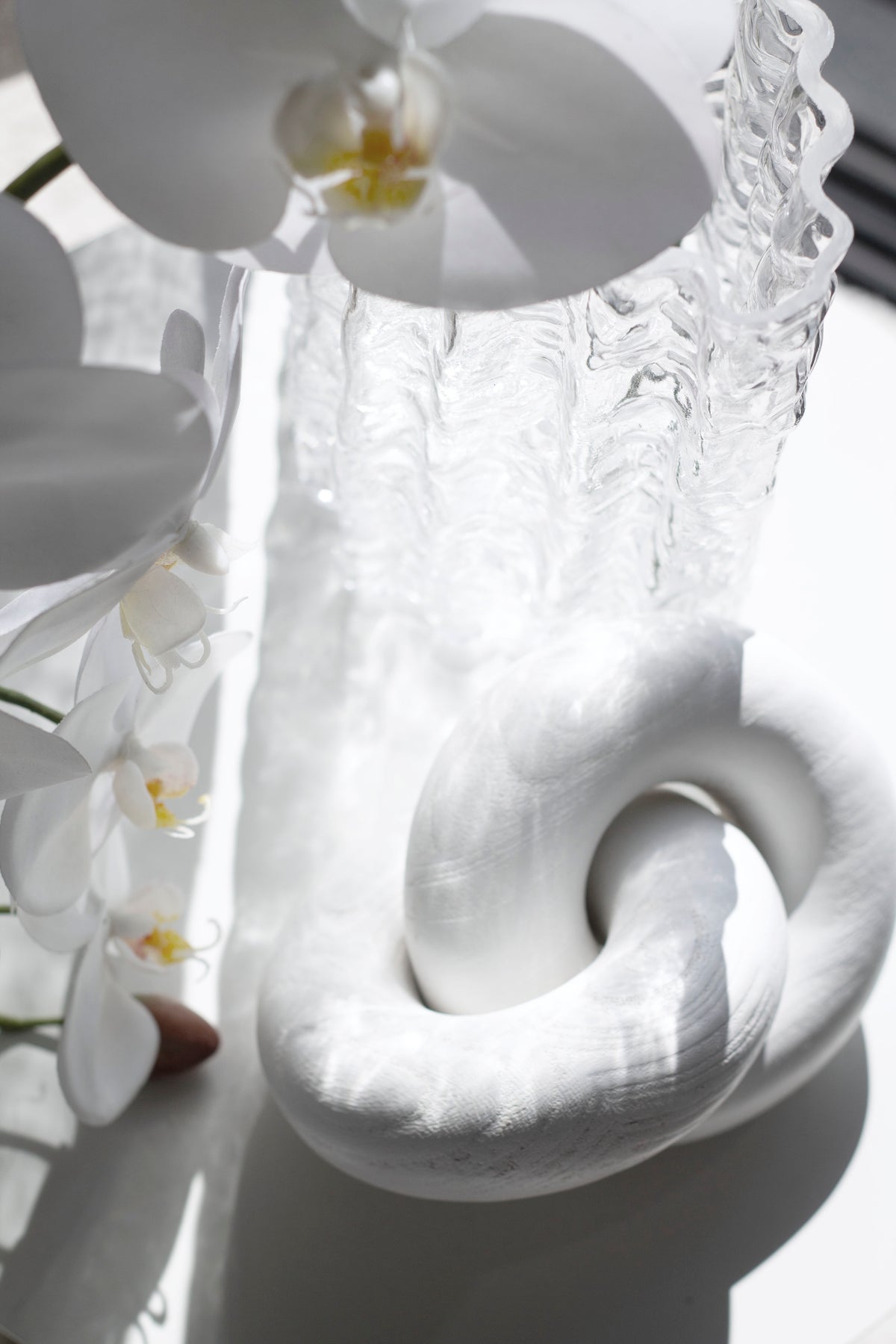 White wooden knot sculpture beside a white orchid in bright reflected light