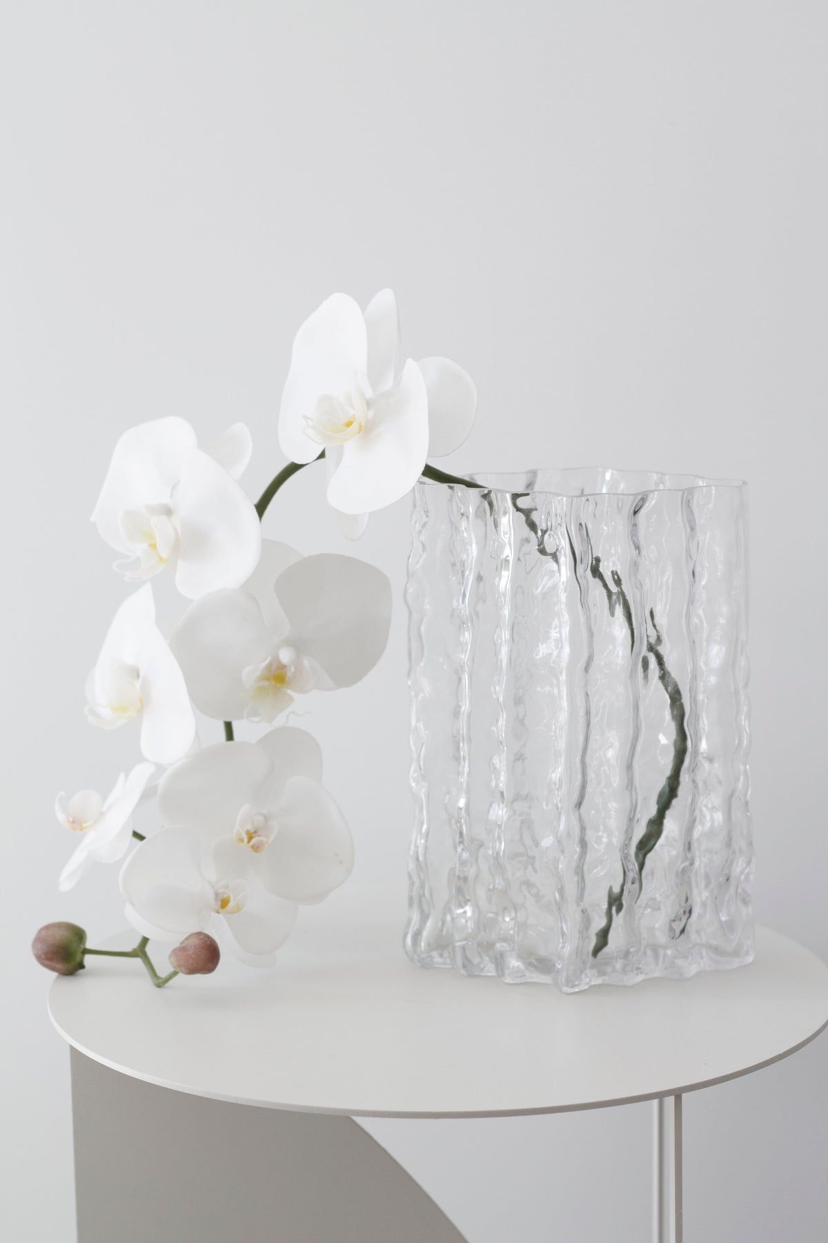 Clear Glacier vase with a white orchid on a round white table, seen side on