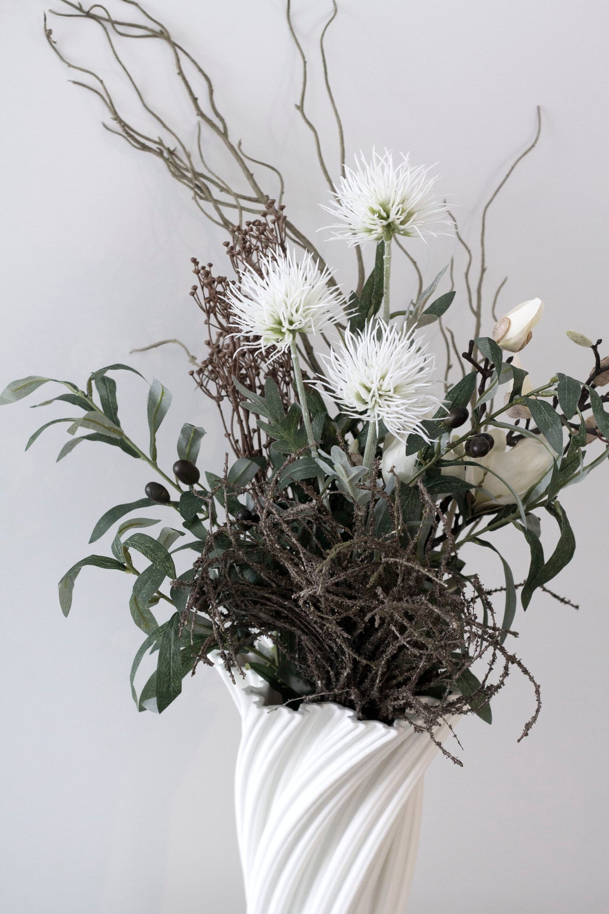 Faux willow branches rising from a white swirl vase with a mixed faux bouquet