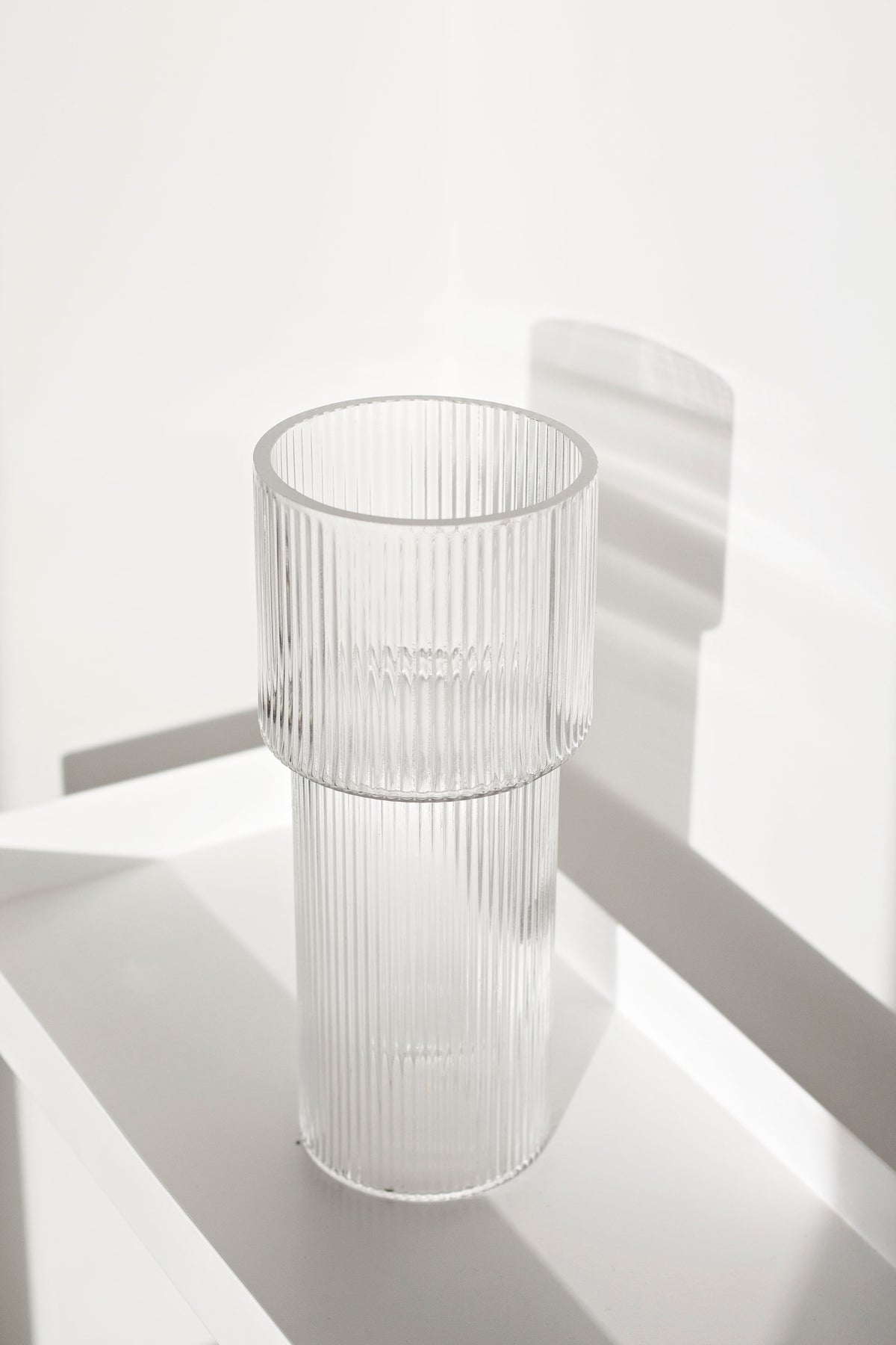 Empty ribbed glass vase on a white tray in bright overexposed light