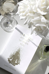 Flatlay of The Unlimited Power Within You by Karin Hadadan with white roses, wine glass, and perfume bottle on a glossy white surface.