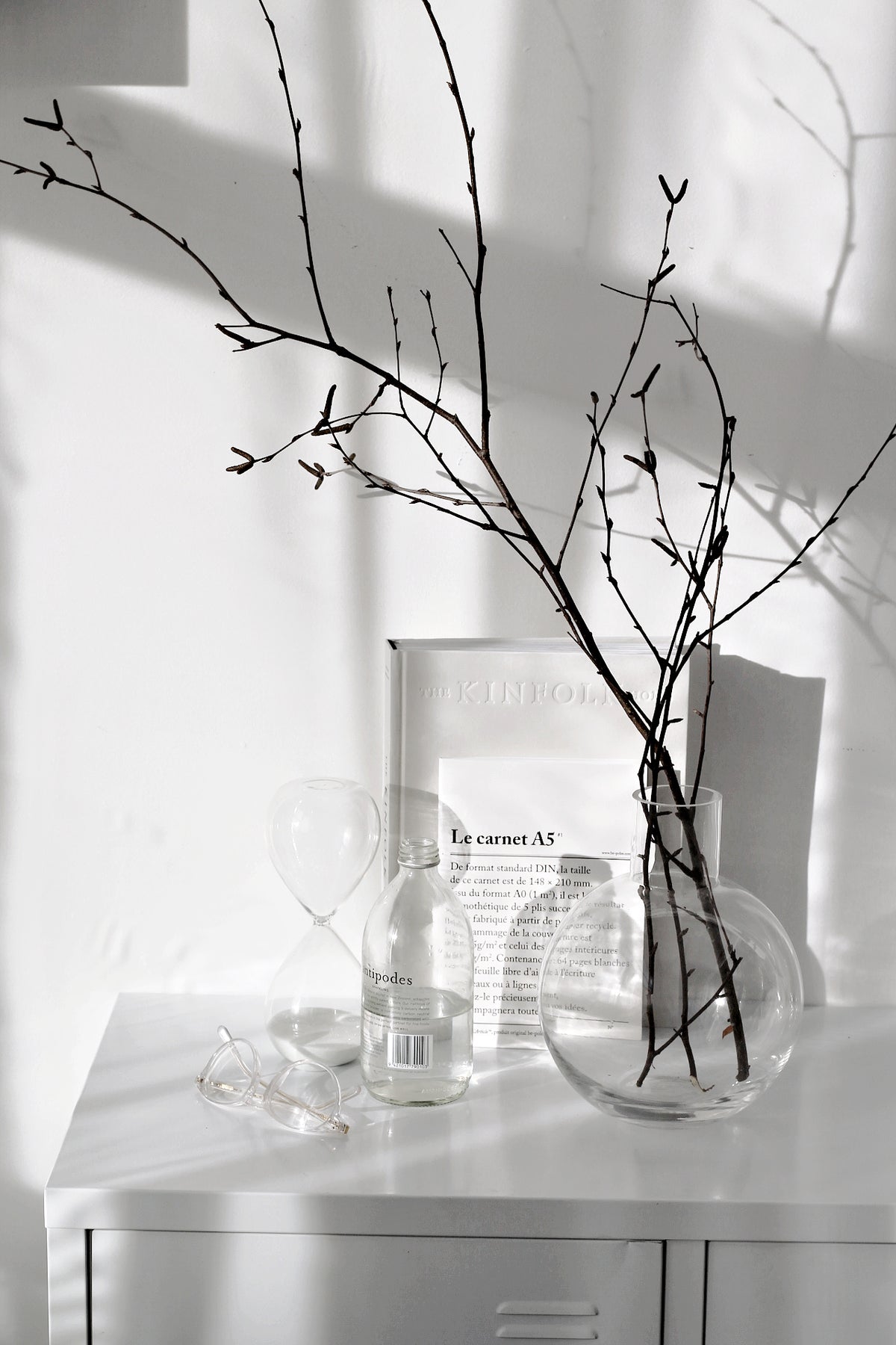 Hourglass resting on its side on a white cabinet beside bare branches in a round glass vase
