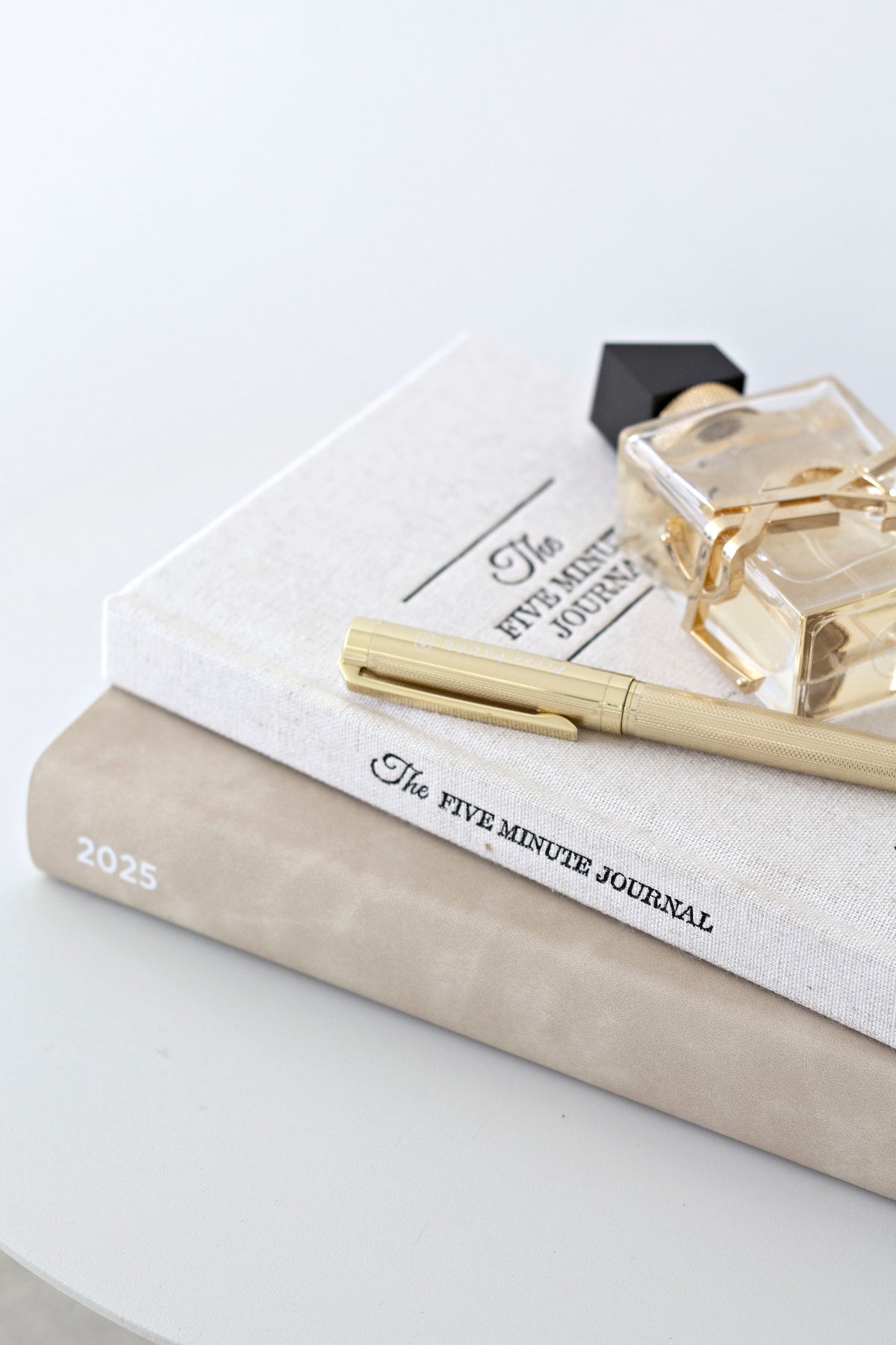Five Minute Journal with a cream pen and a perfume bottle on a stack of books