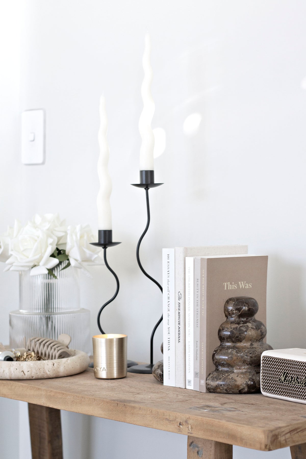 Black Hera holders with twisted tapers on a rustic timber console with books and white blooms