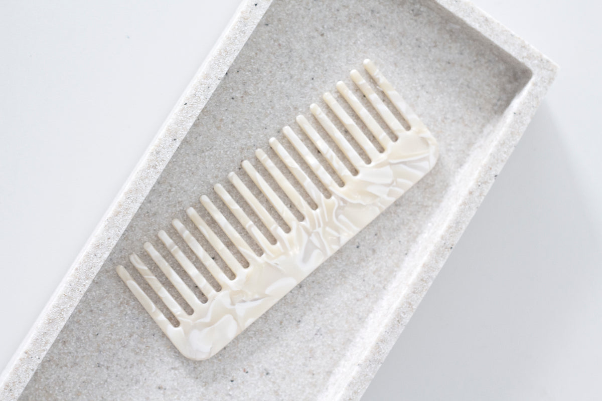 Pearl acetate comb in a speckled stone tray, showing the wide tooth spacing
