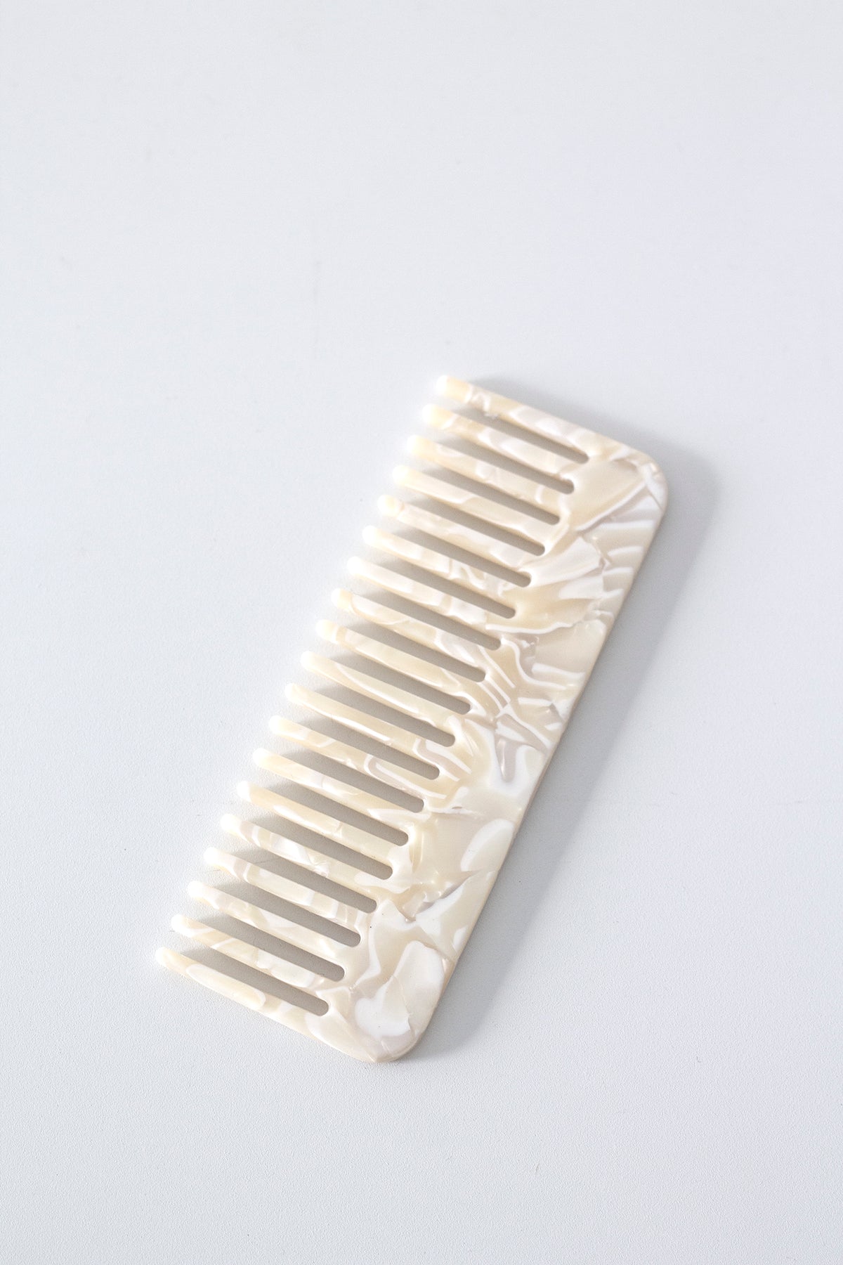 Pearl acetate comb on a pale grey background, showing the marbled finish