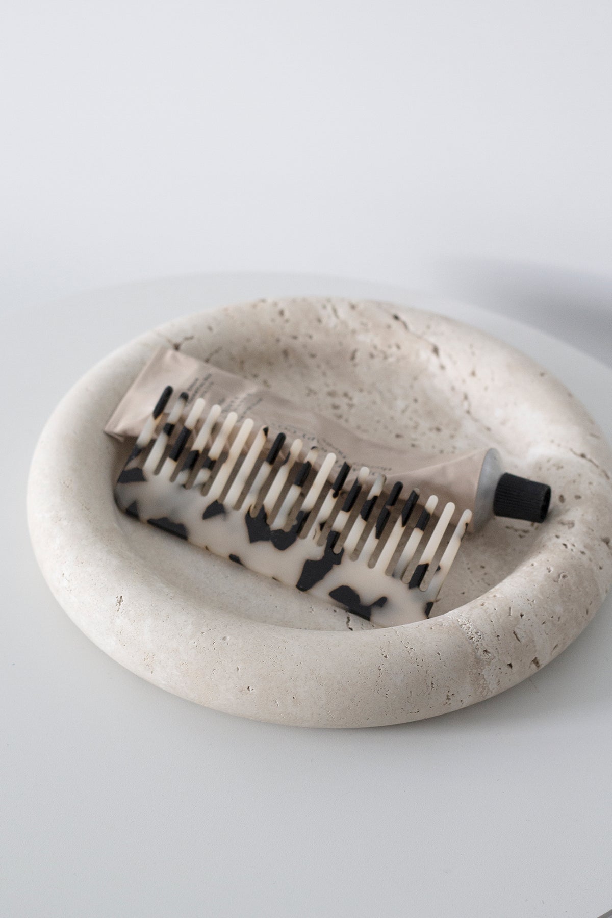 Black and white acetate comb in a round travertine dish on a pale surface