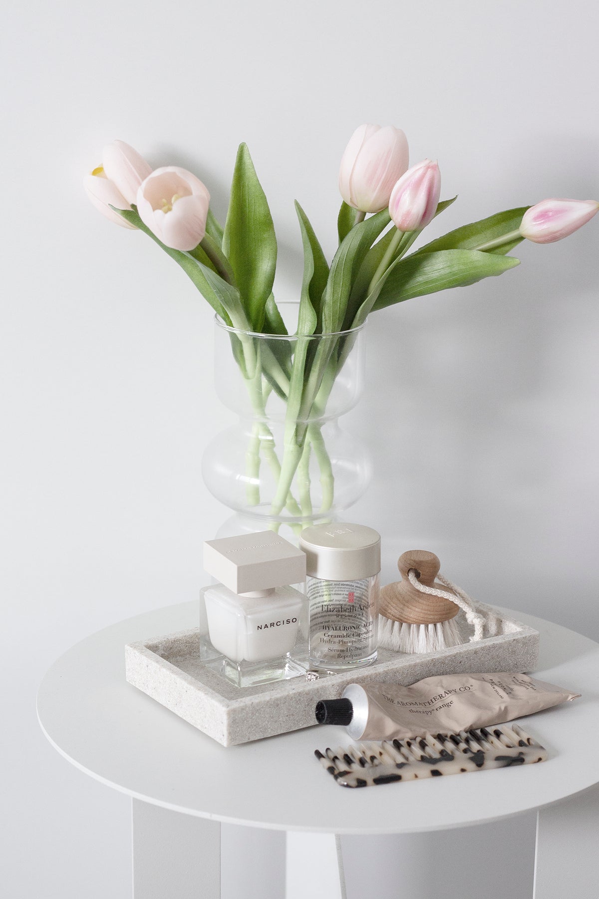 Pale pink faux tulips in a glass vase on a side table with stacked books
